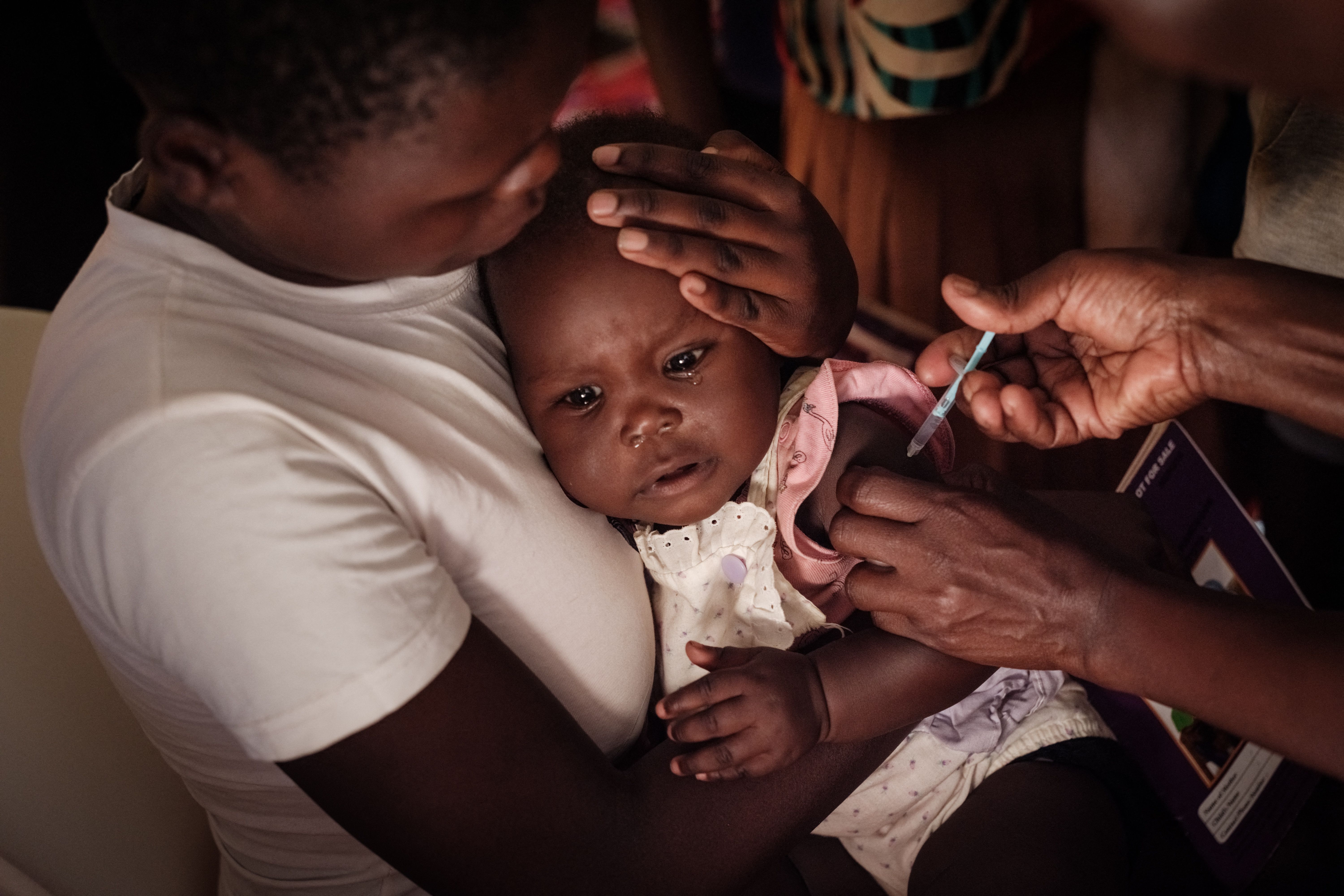 A child held tightly by its mother receives a malaria vaccine.