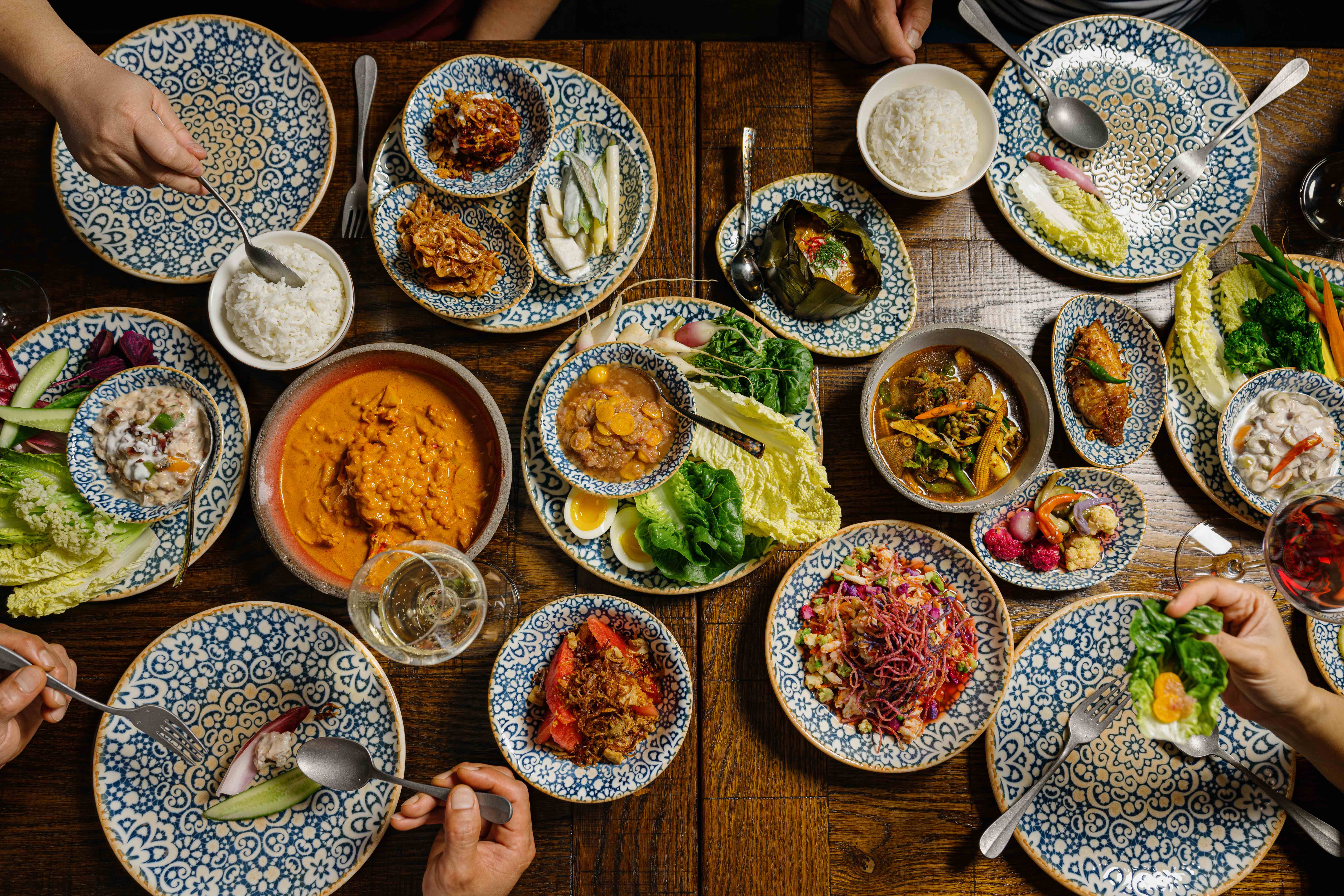 Thai food is displayed in various blue and white bowls on a wooden table.
