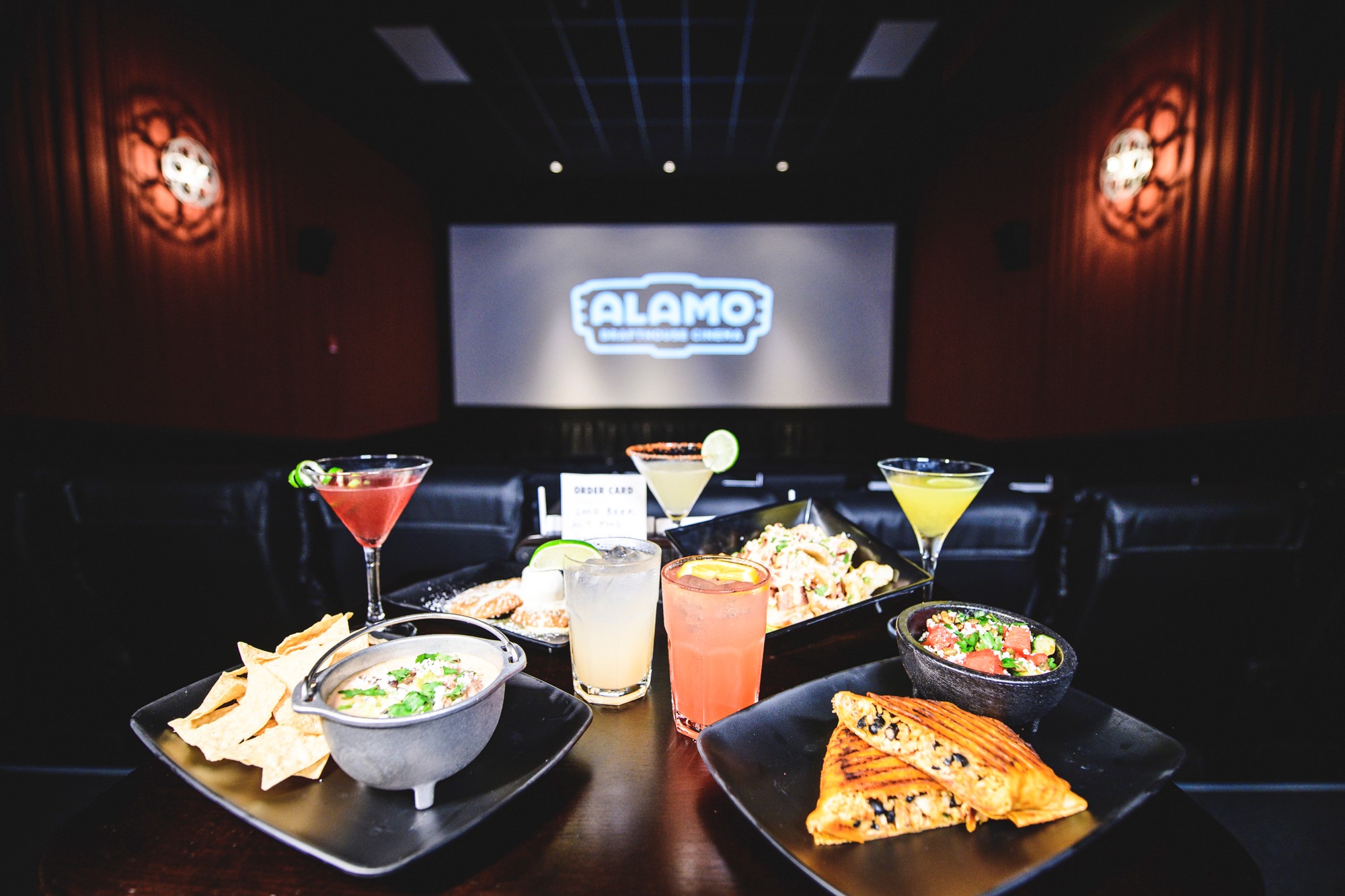A spread of food and drinks laid out in a movie theater with a theater screen in the background.