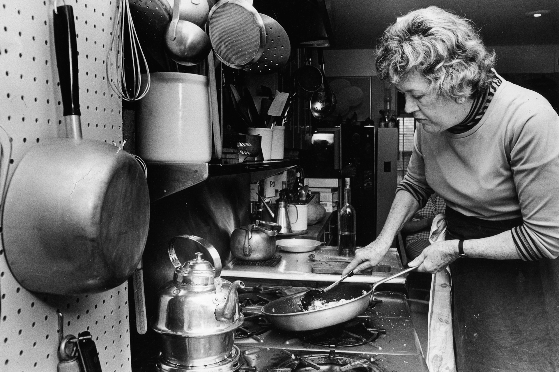 A black and white photo of Julia Child cooking on a gas stove