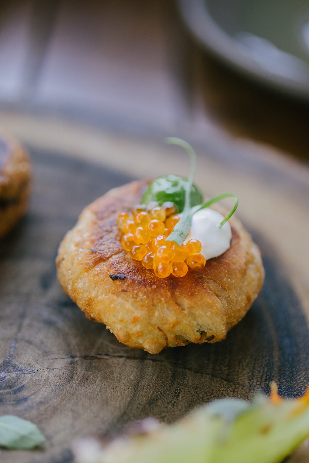 A round knish with creme fraiche and salmon roe, on a d plate.