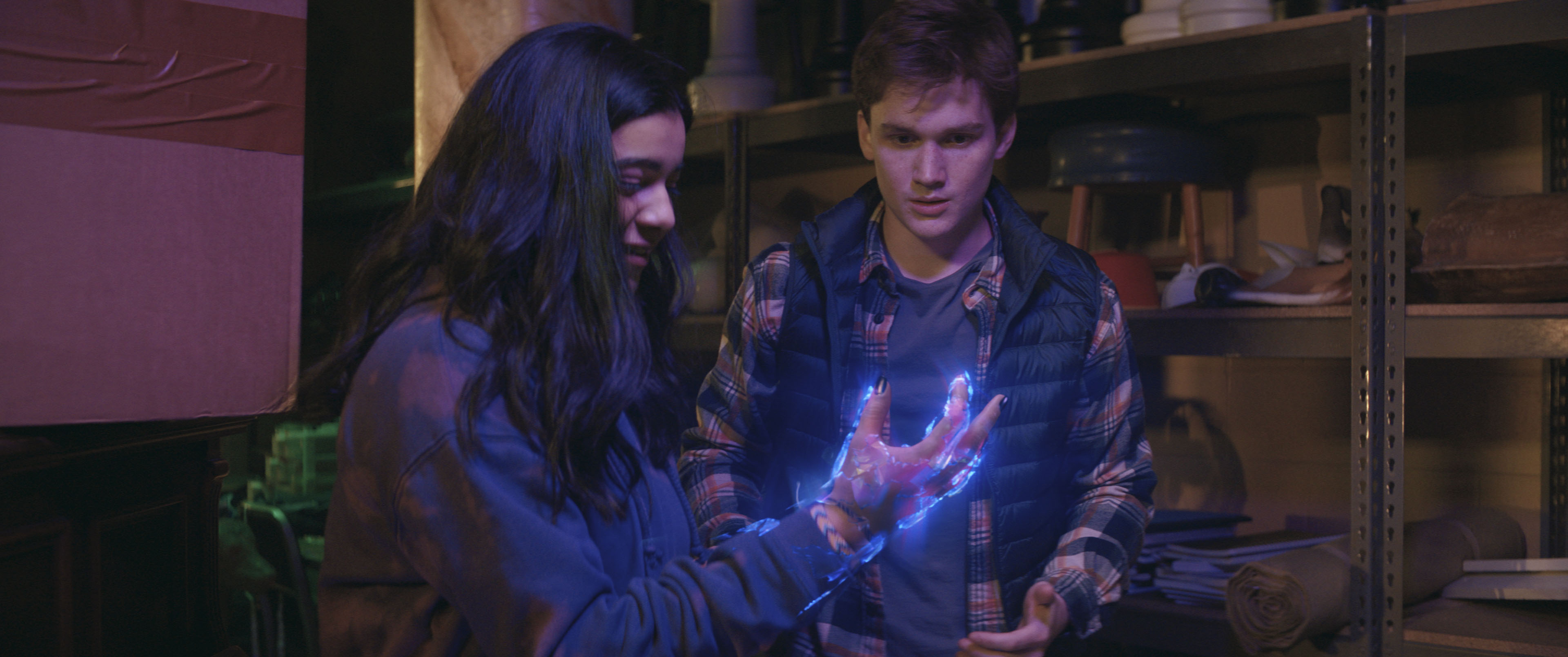 (L-R): Iman Vellani as Ms. Marvel/Kamala Khan, holding up her hand, which is glowing with strange energy, and Matt Lintz as Bruno in Ms. Marvel.