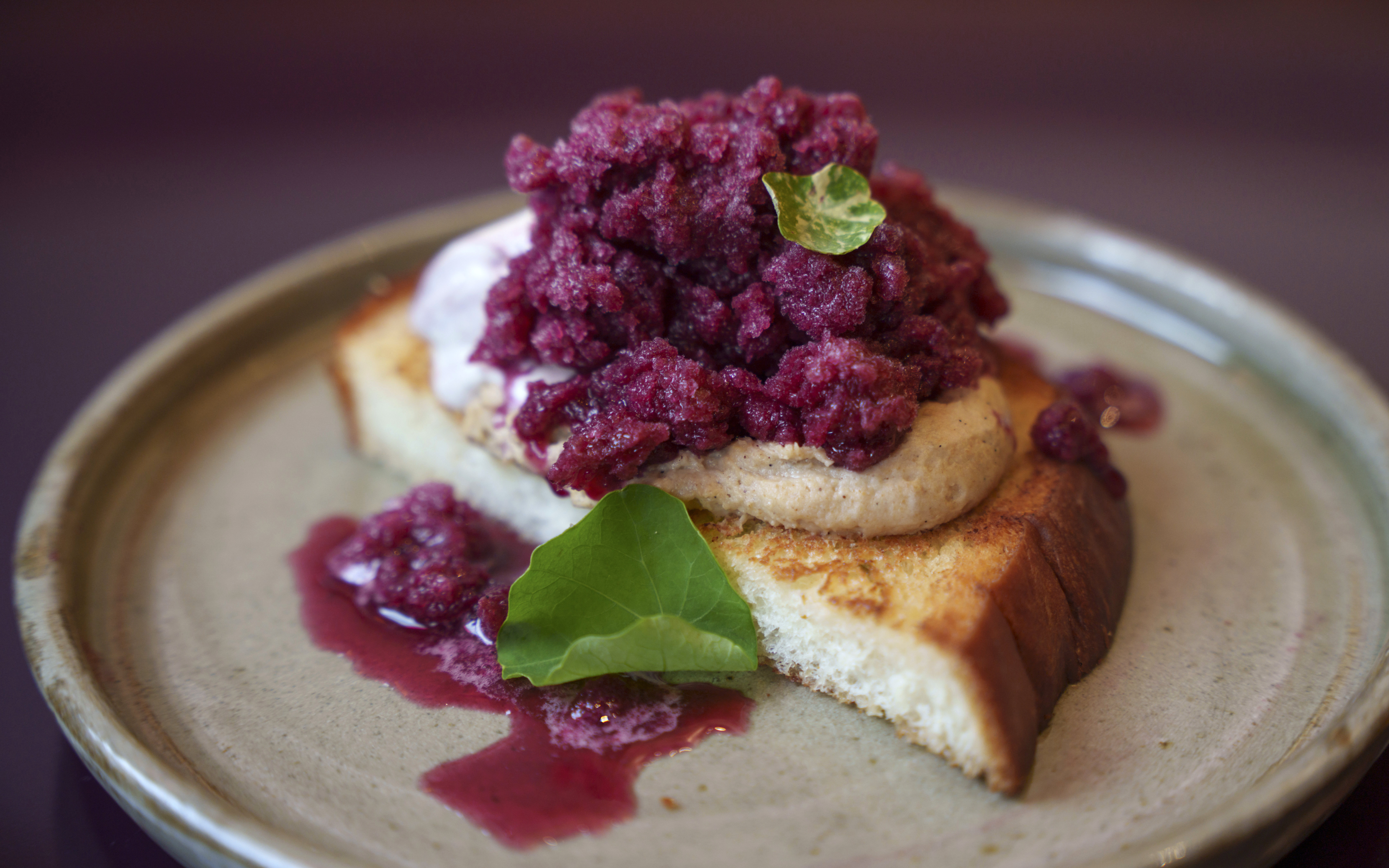 A slice of milk toast topped with sesame mousse and purple grape ice cream on a round beige plate.