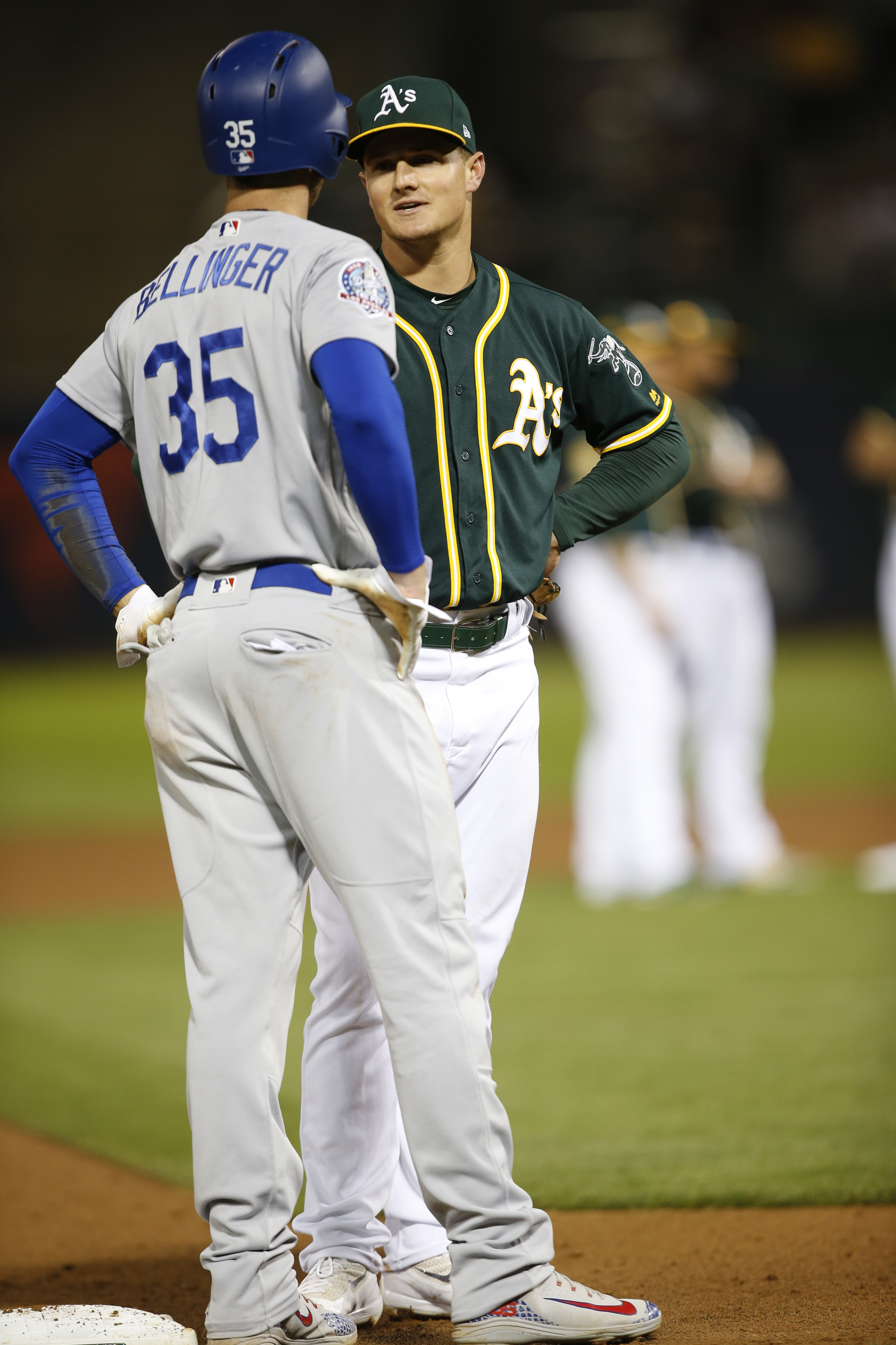 Cody Bellinger with a batting helmet standing on third base talking to Matt Chapman. 