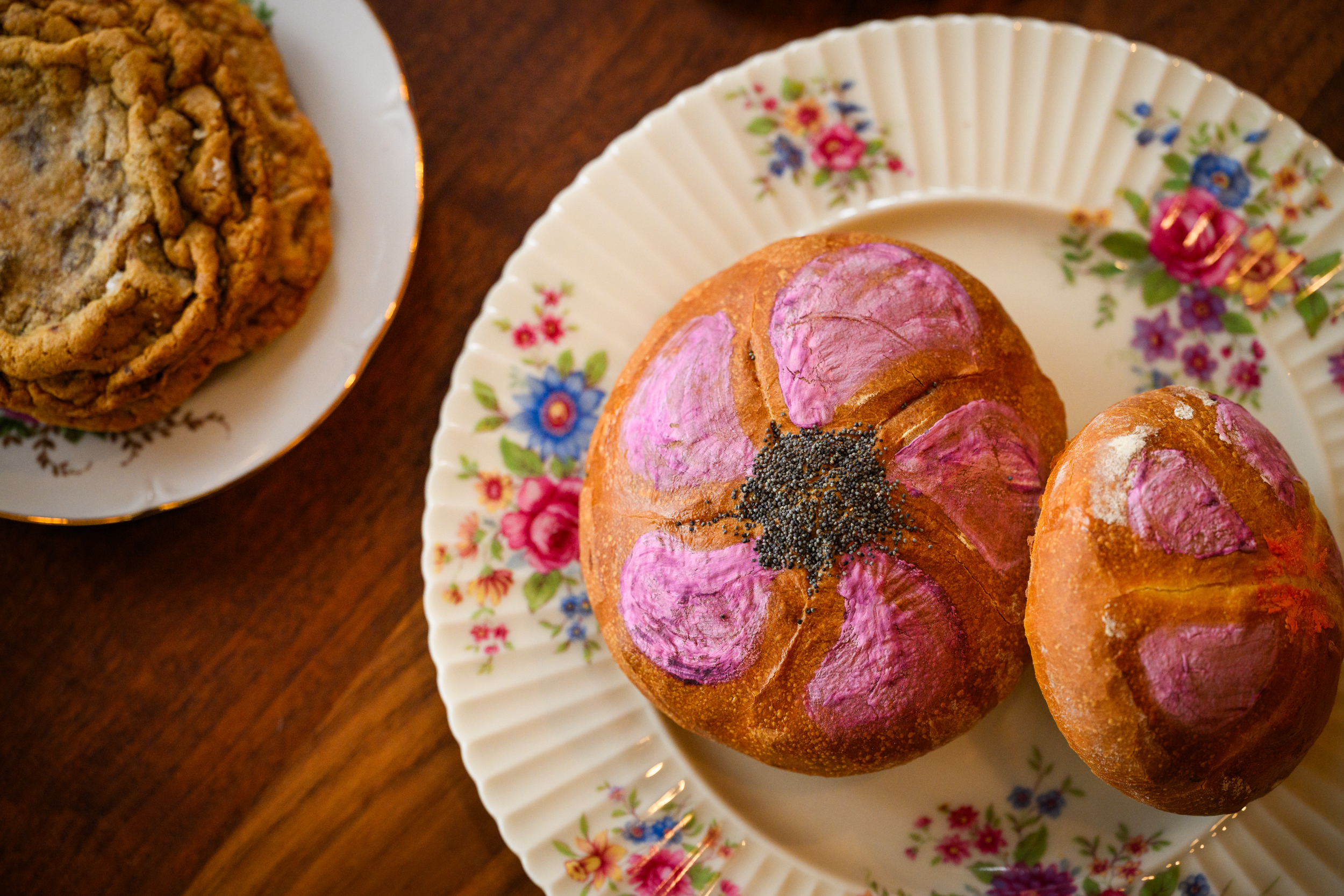 Two Kaiser rolls with pink frosting sit on a floral plate at Flour Bloom.
