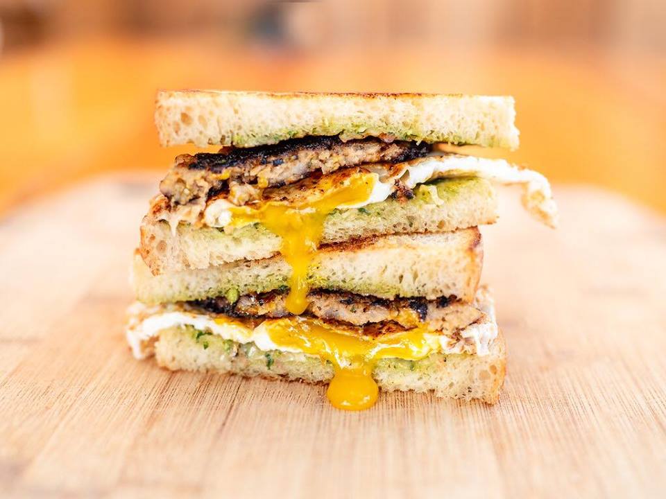 Two egg sandwiches sit on top of each other with a crisp sausage patty and green pesto.