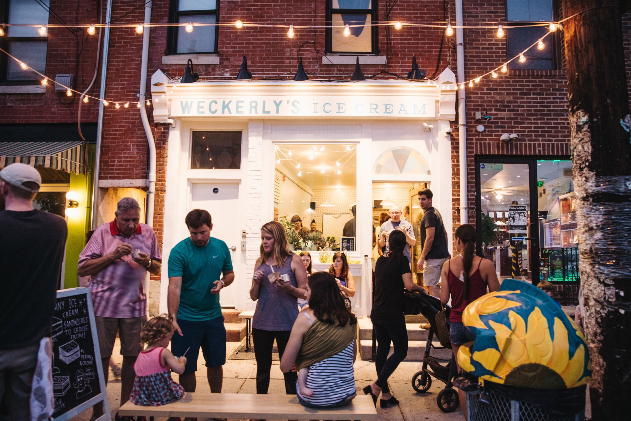 A group of people outside an ice shop enjoying scoops in the evening. 