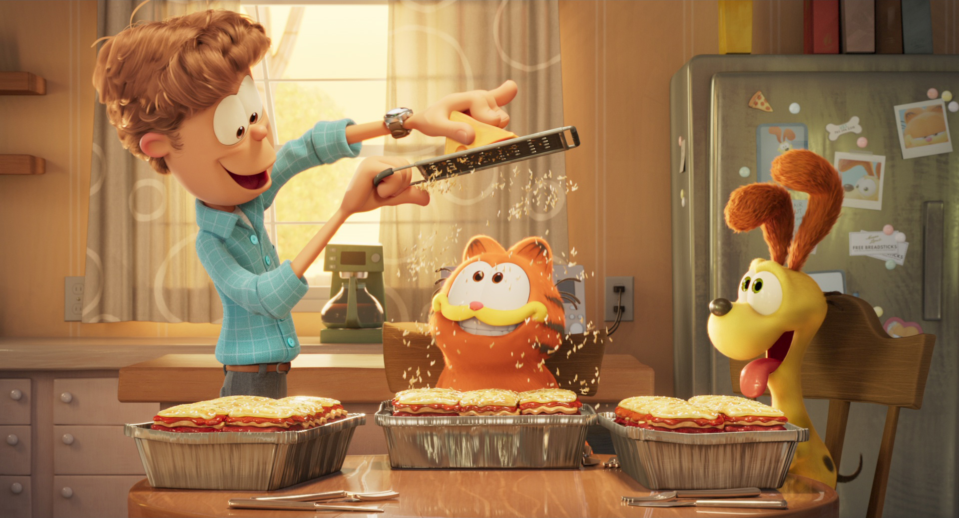 Jon Arbuckle grates Parmesan cheese over Garfield’s lasagna while Odie watches in a still from The Garfield Movie
