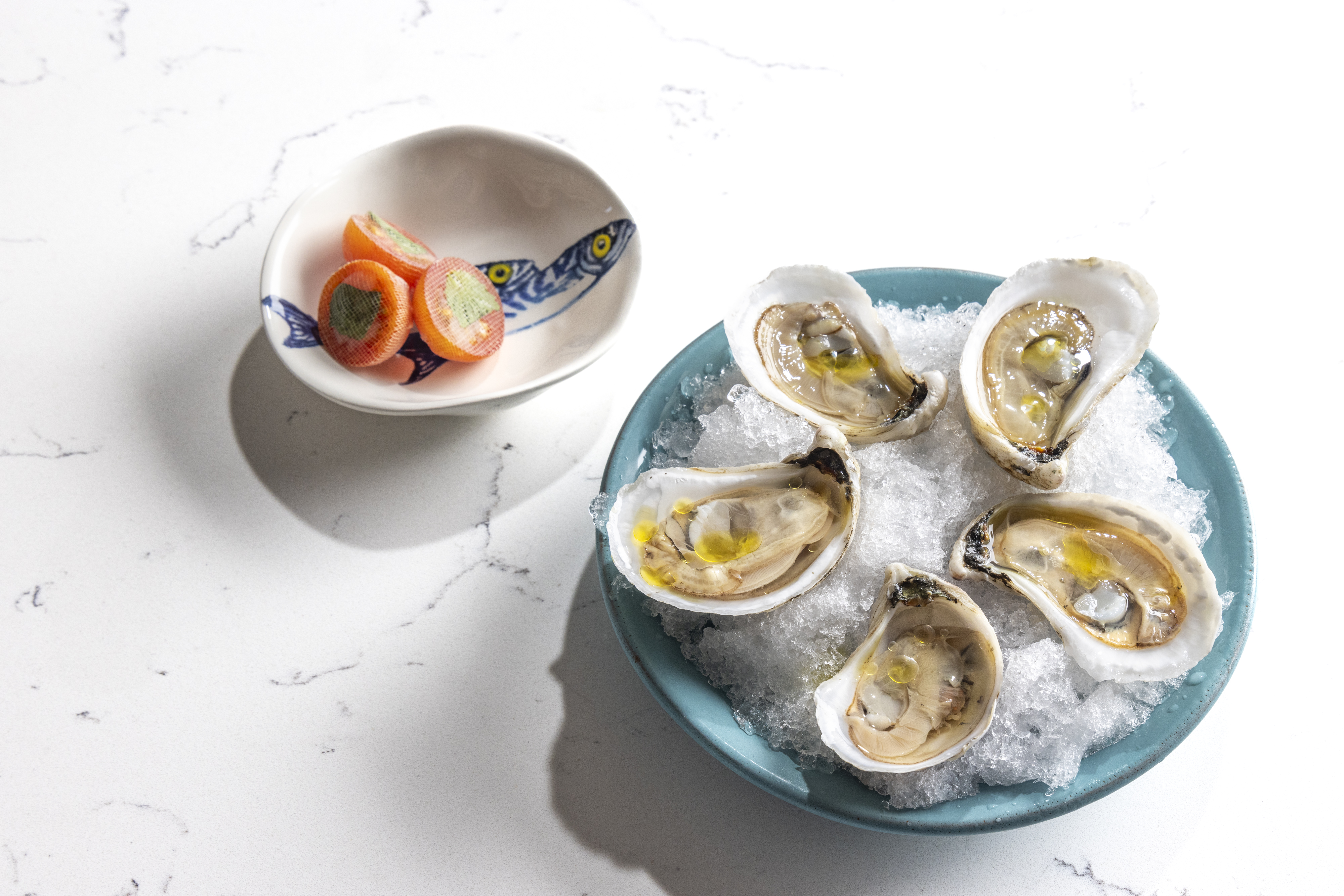 Five half-shell oysters on ice, next to a bowl of tomatoes.&nbsp;