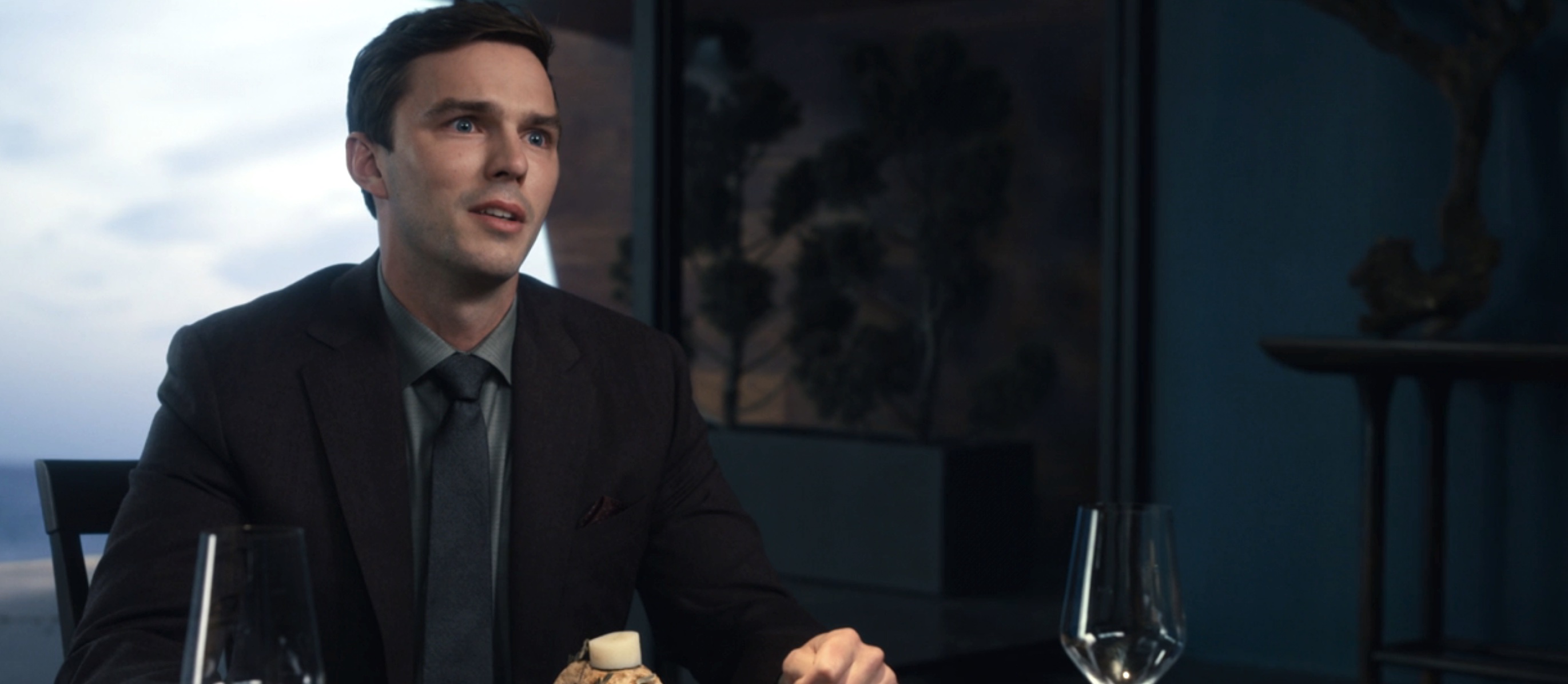 Nicholas Hoult’s Tyler, dressed in a suit and tie, tears up as a chef off screen describes his meal in The Menu