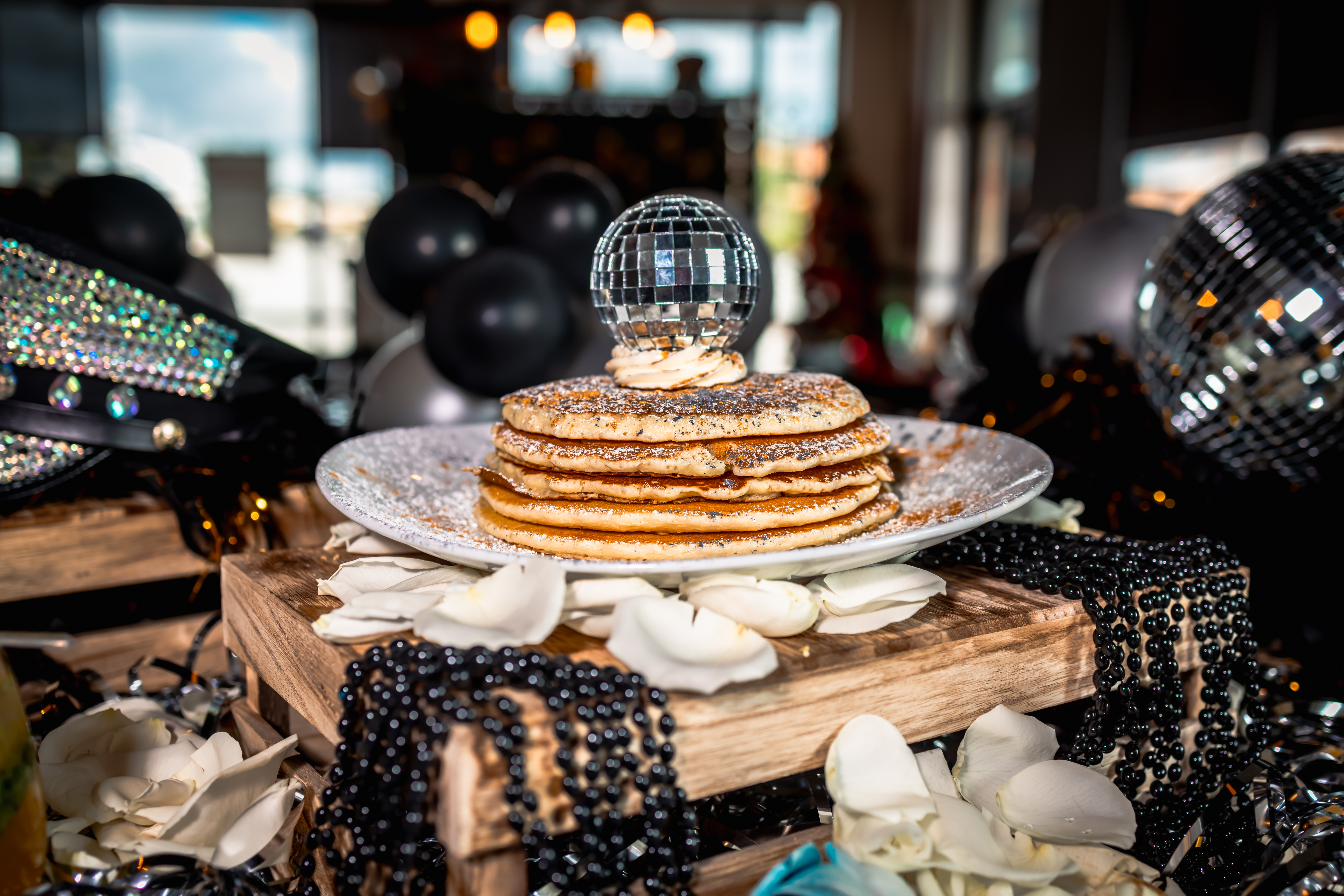 A stack of pancakes topped with glitter, whipped cream, and a sparkling disco ball.