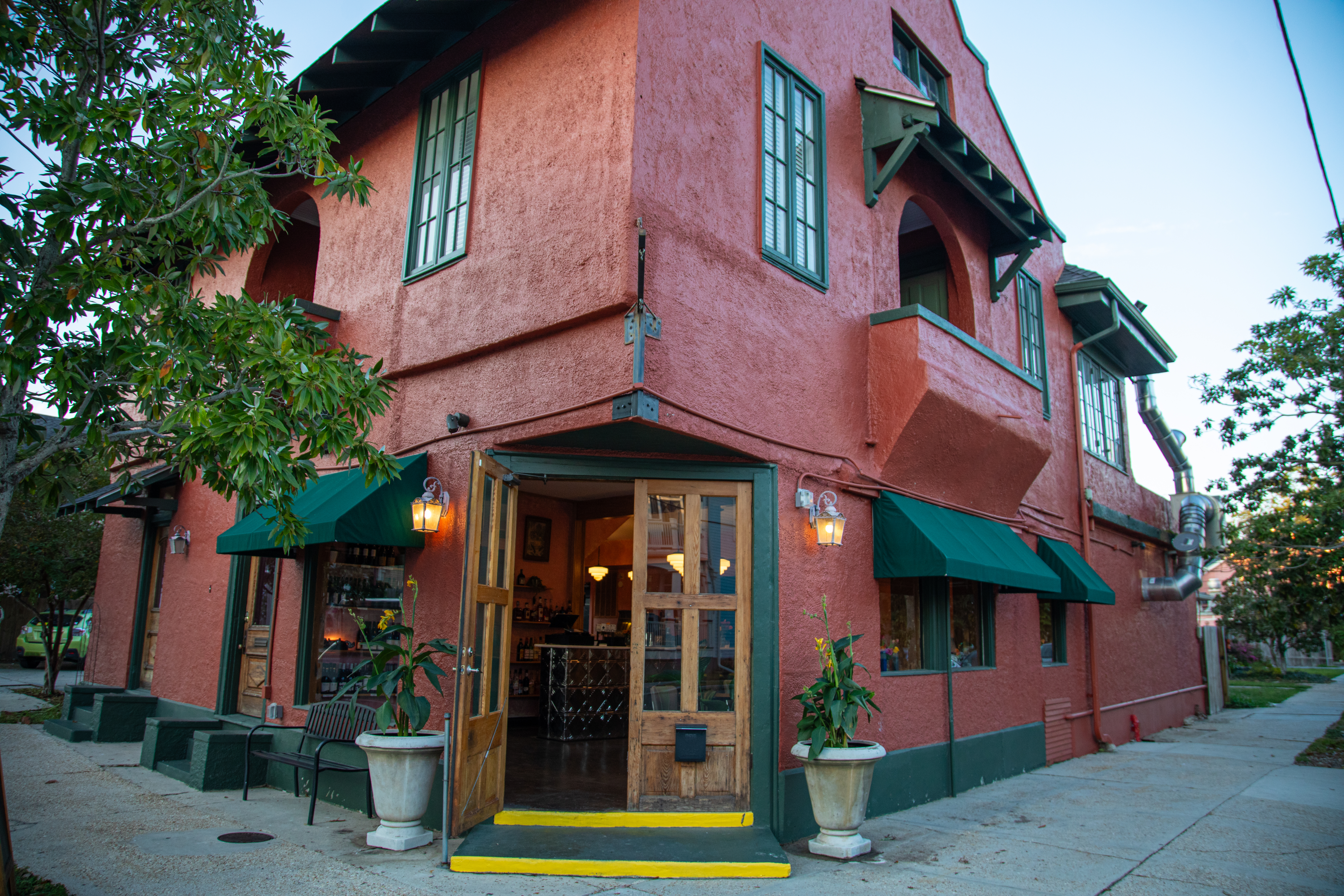 A corner building with a muted red facade and green awnings and window trim. 