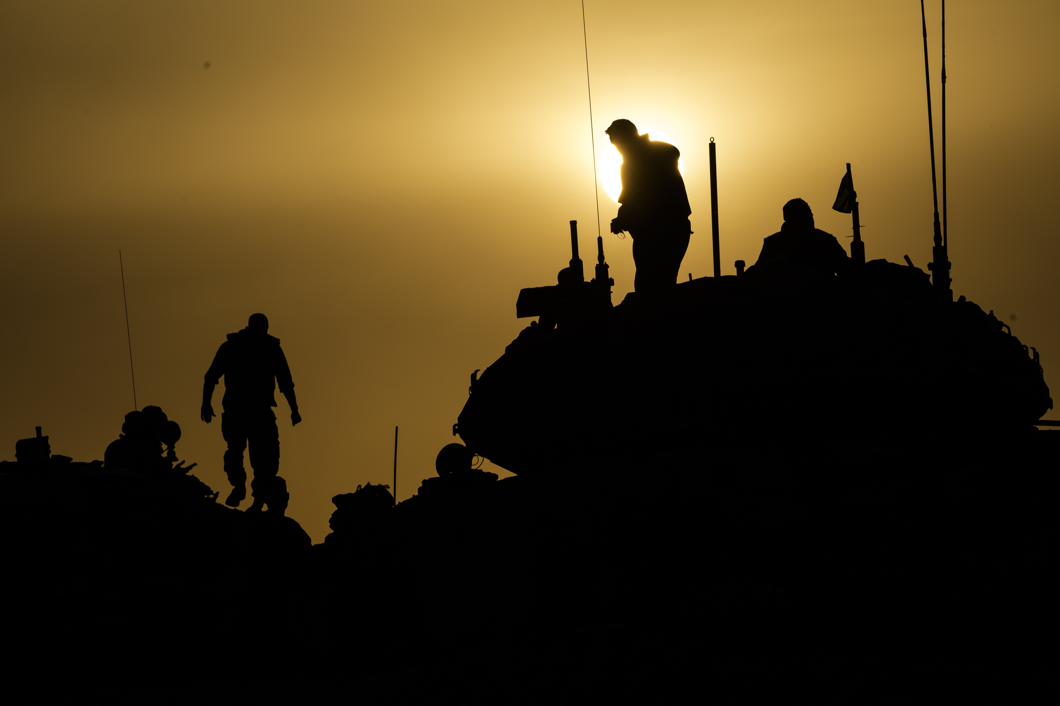 The black outline of an armored vehicle or tank and several human figures is silhouetted against a hazy, yellowish sky.