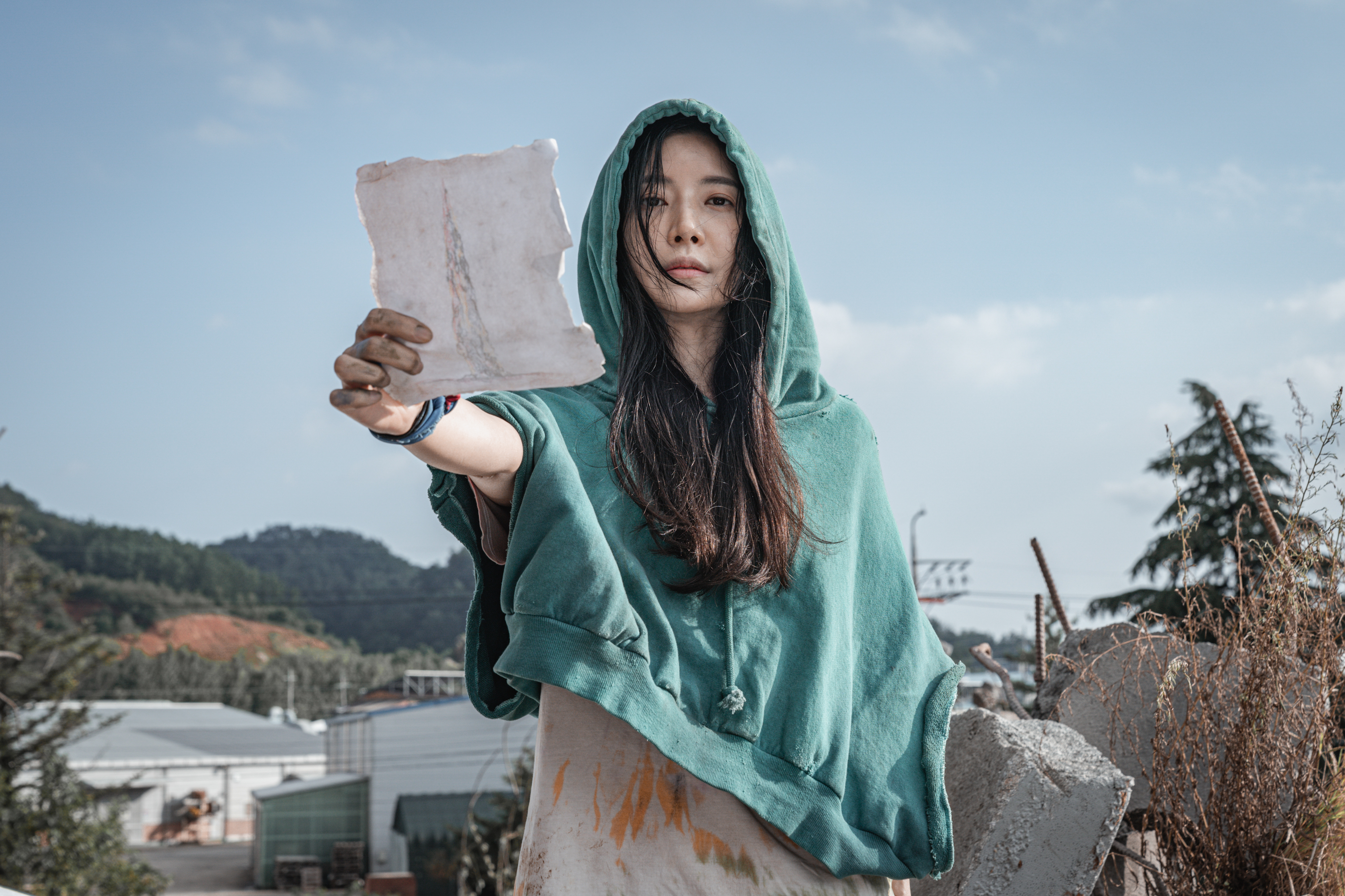 A woman in a green hoodie holds up a piece of paper in Sweet Home.