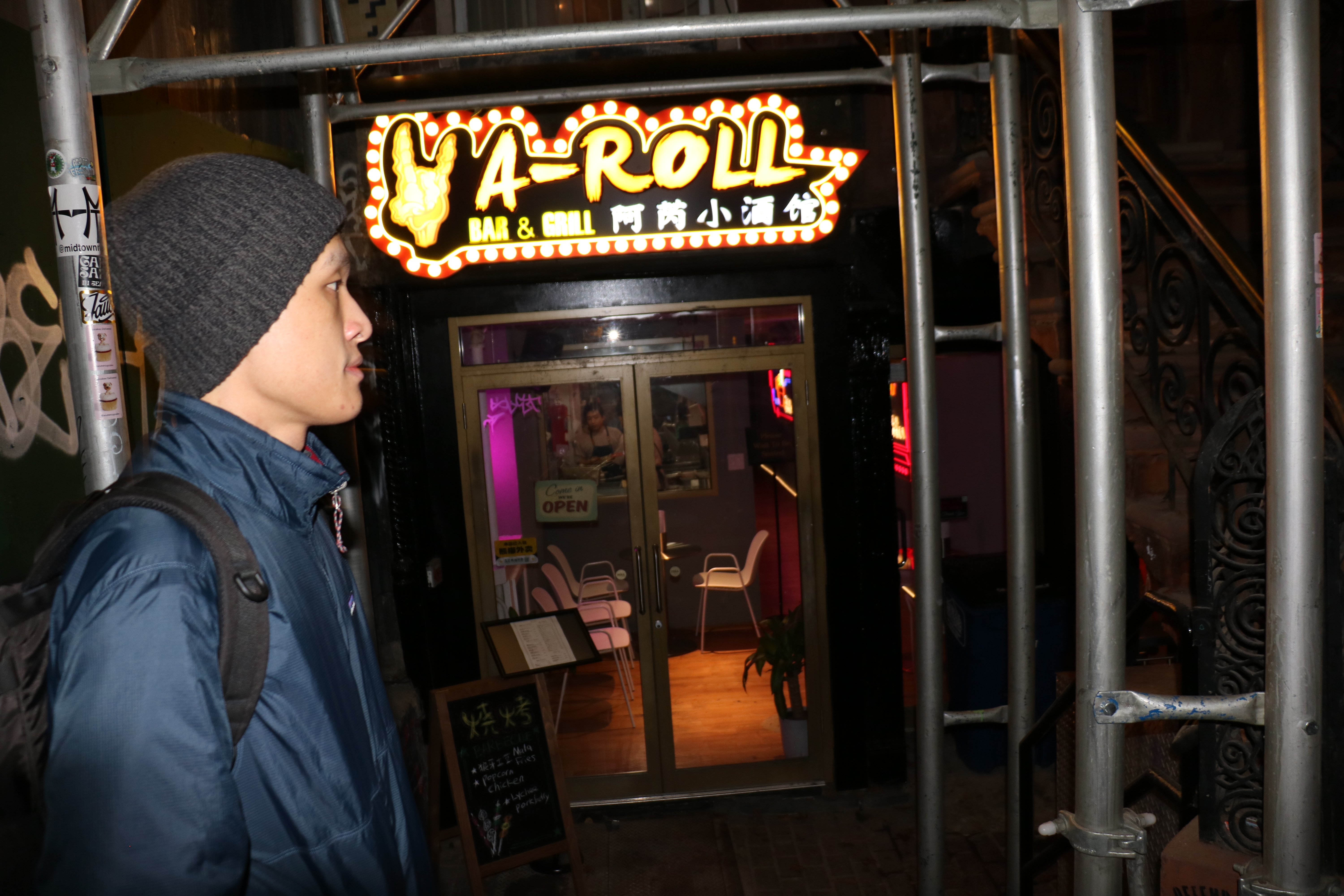 A person walks in front of a skewer shop set slightly below street level.