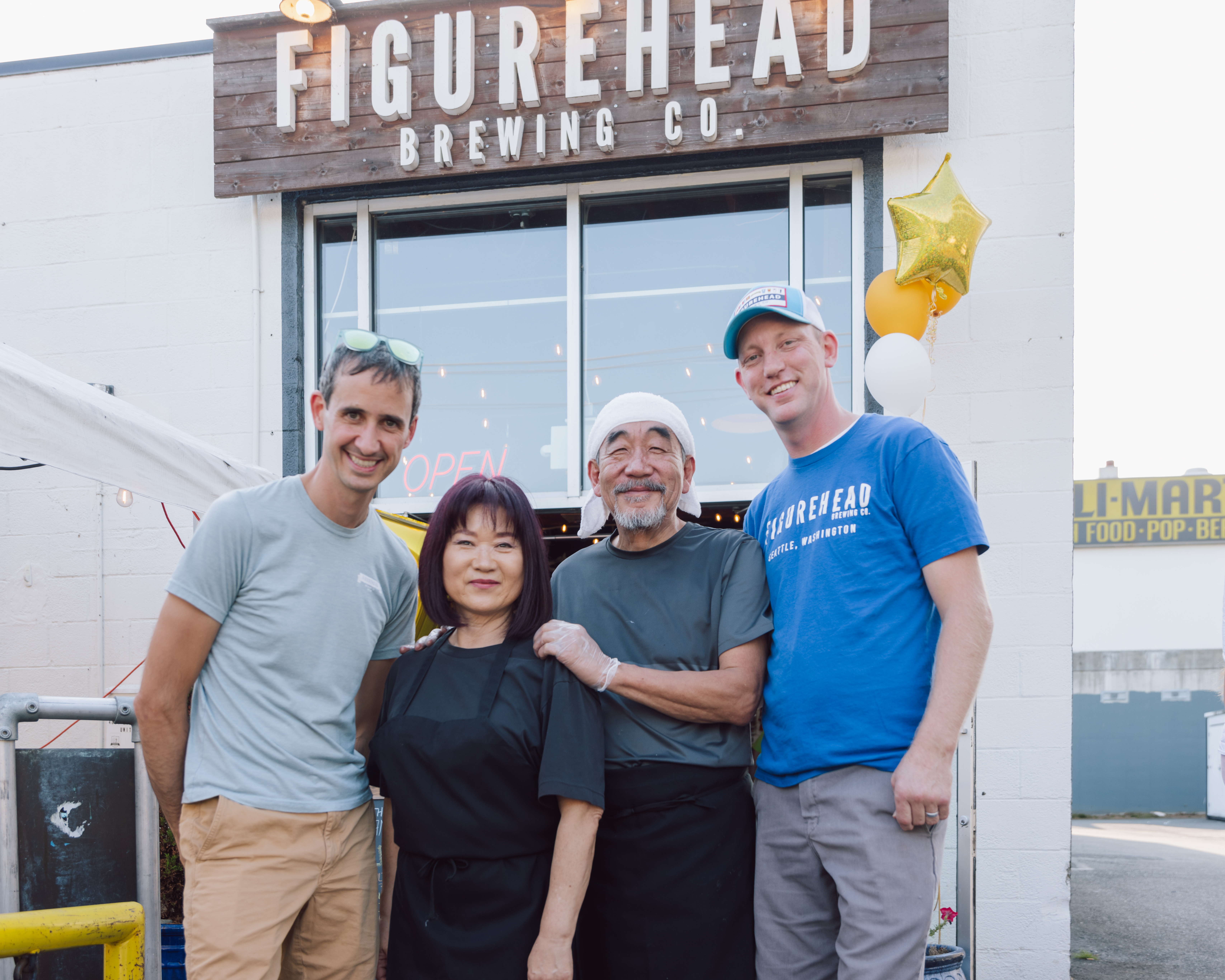 Two white men, an Asian man, and an Asian woman pose in front of a sign that says, “Figurehead Brewing Co.”