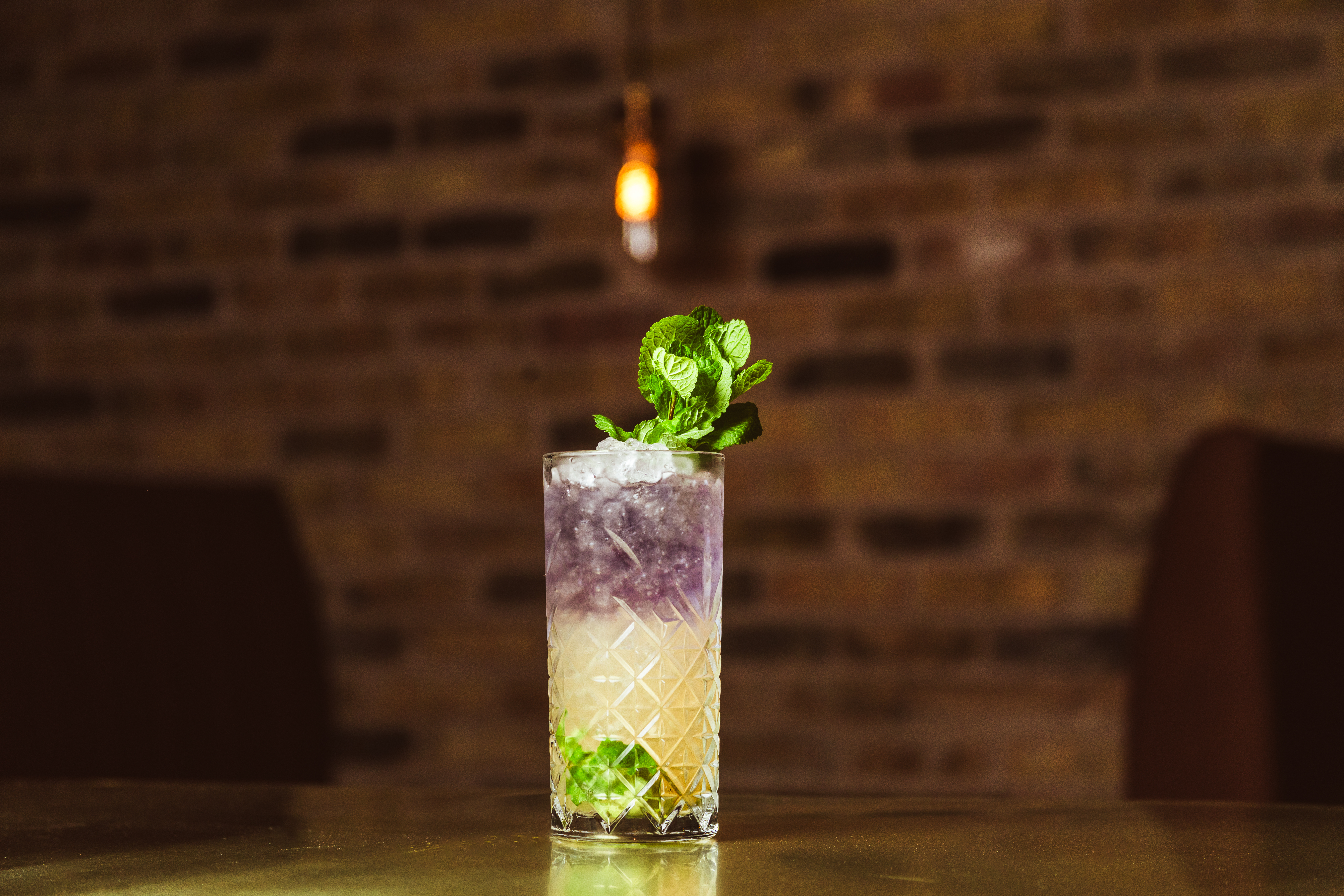 A cocktail with purple and yellow liquid in a clear glass with ice and green herbs.