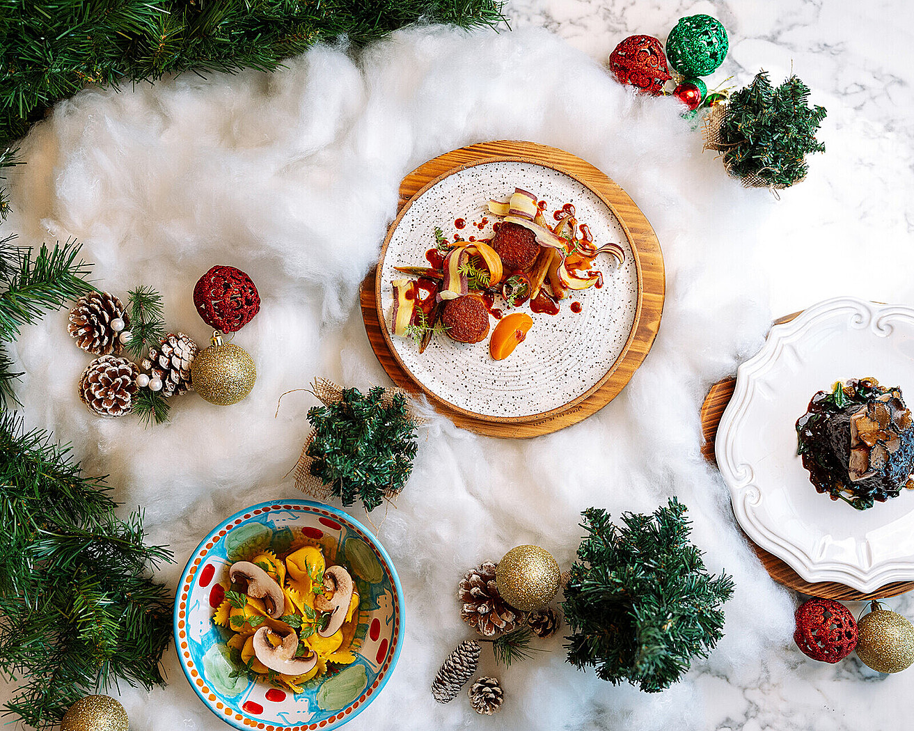 Several dishes sitting a tufted cloud of cotton meant to look like snow surrounded by pine cones, christmas ornament balls, mistletoe, and fir branches