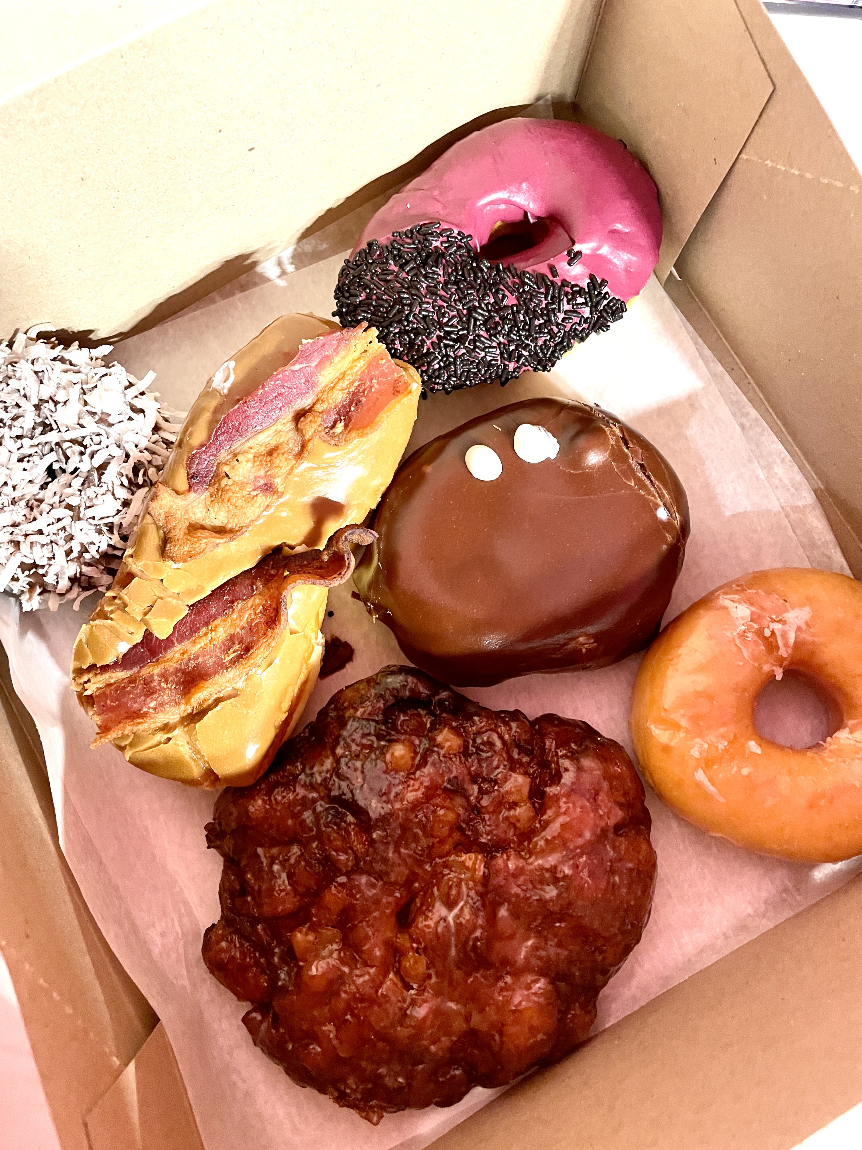 A box holds doughnuts, fritters, and a maple bacon bar.