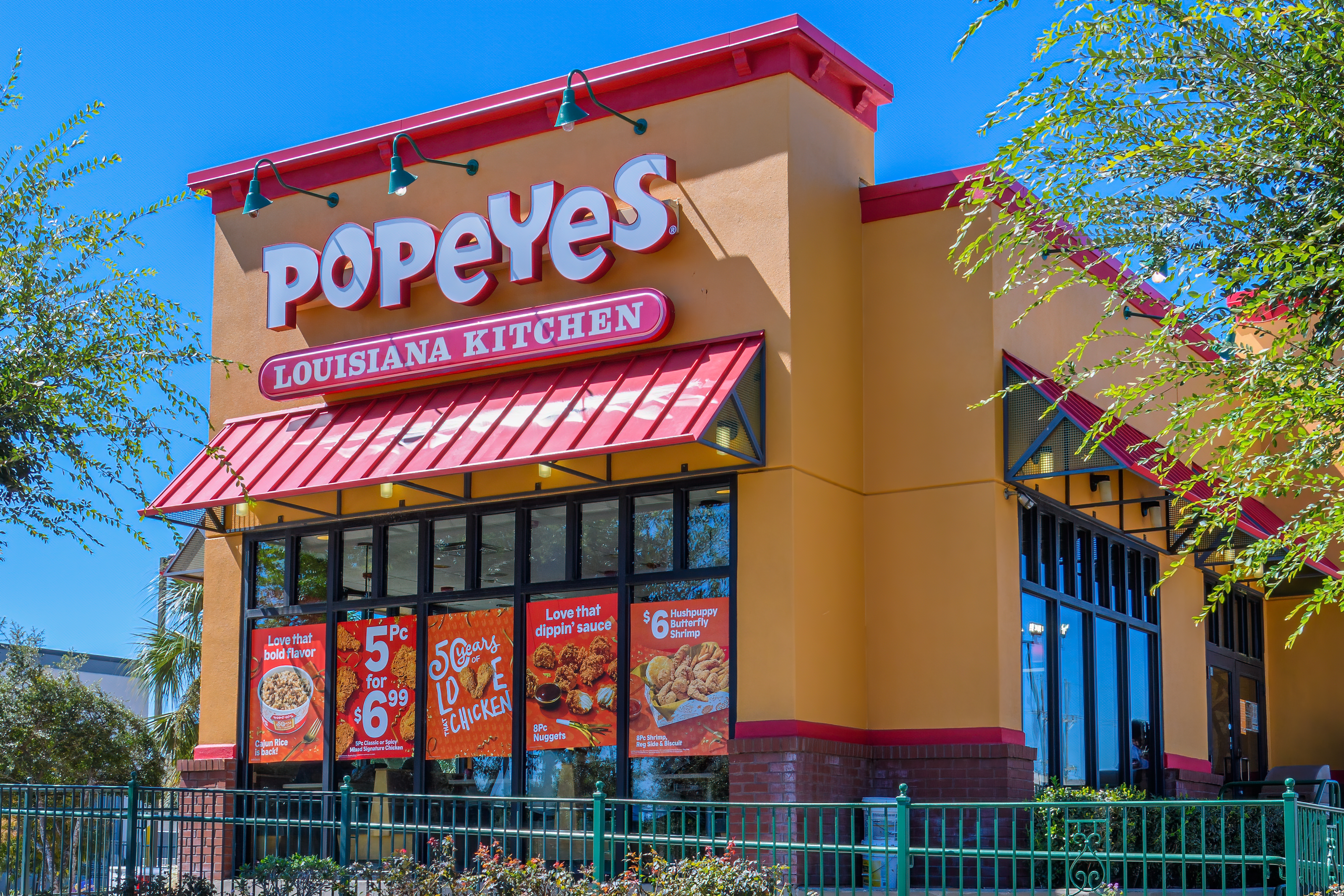 A building with an orange and red color scheme with a large sign reading “Popeyes Louisiana Kitchen.”