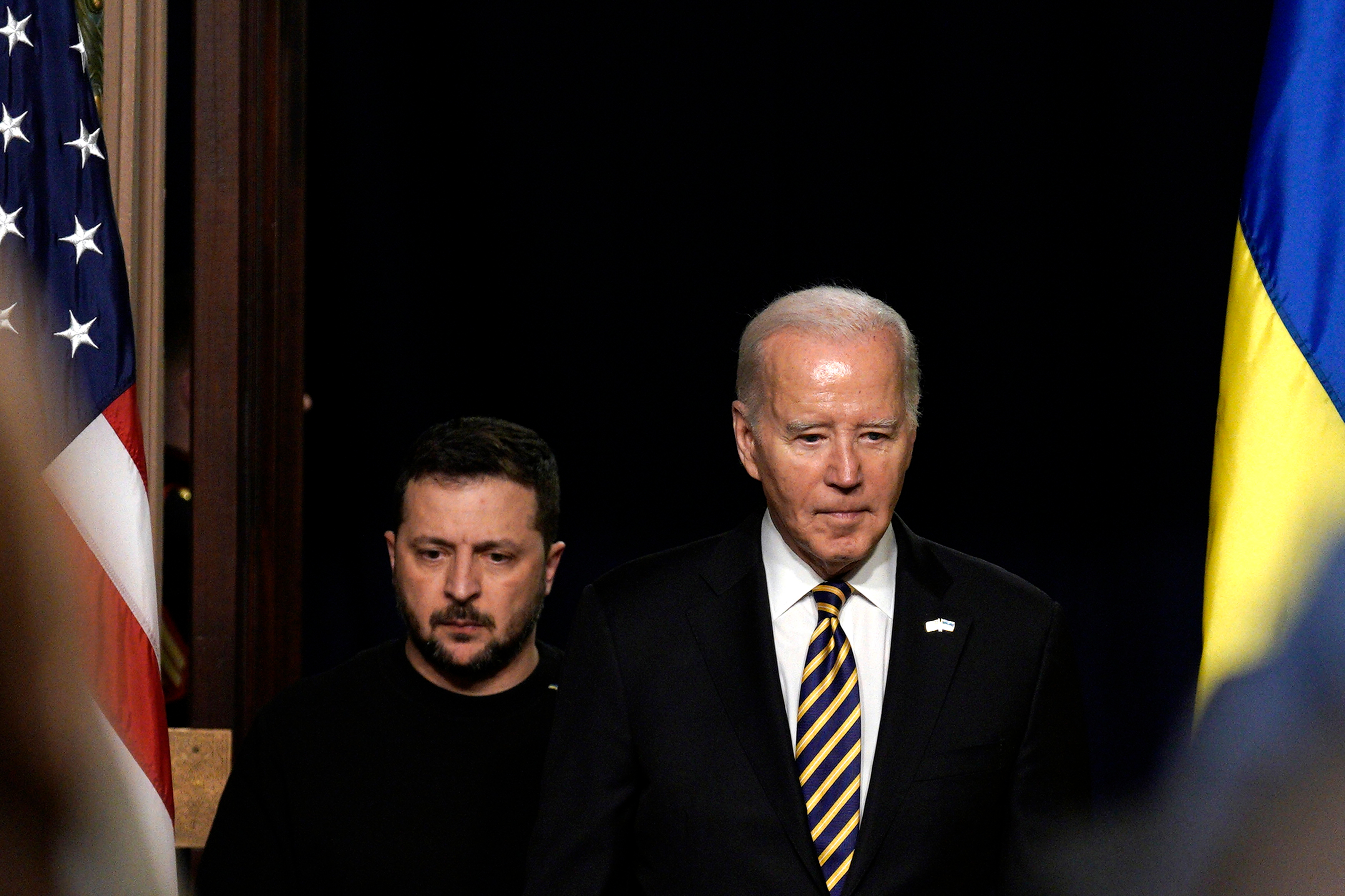Biden and Zelensky enter a room, with the US and Ukraine flags on either side of them.