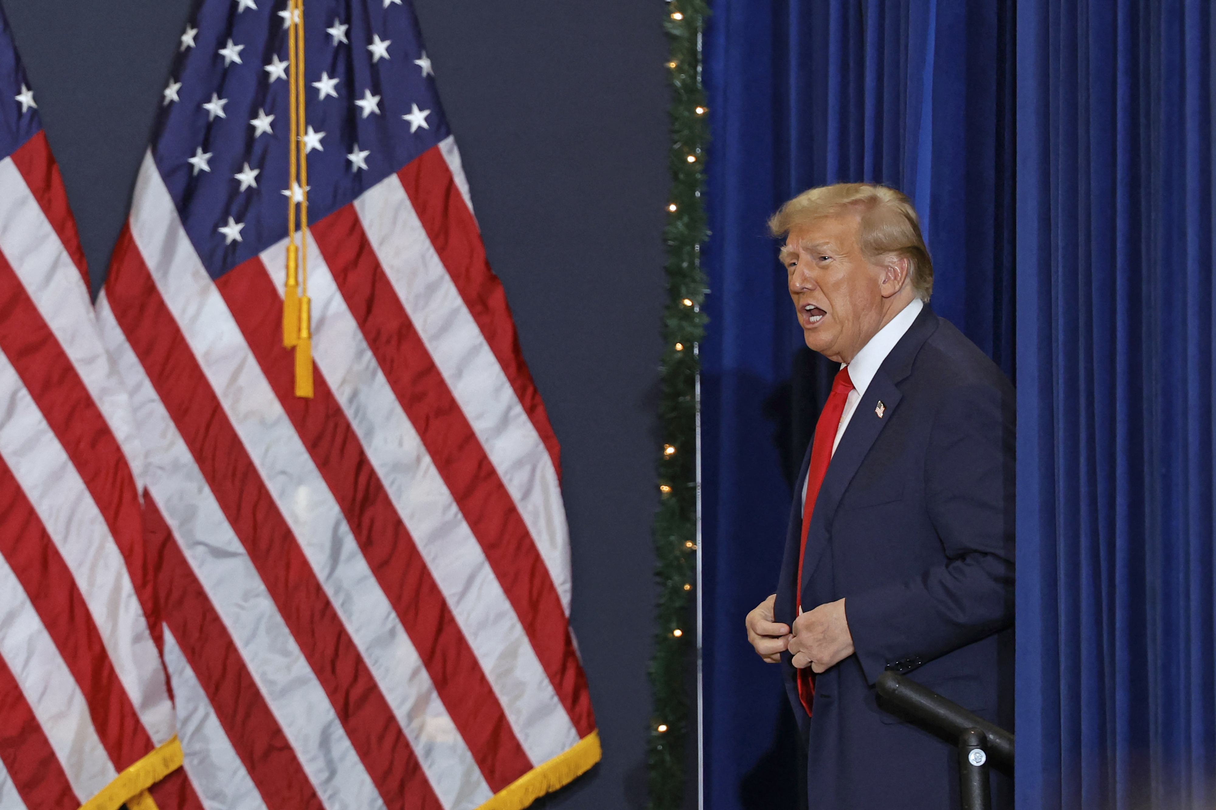 Donald Trump walking onto a stage with large American flags as decoration.