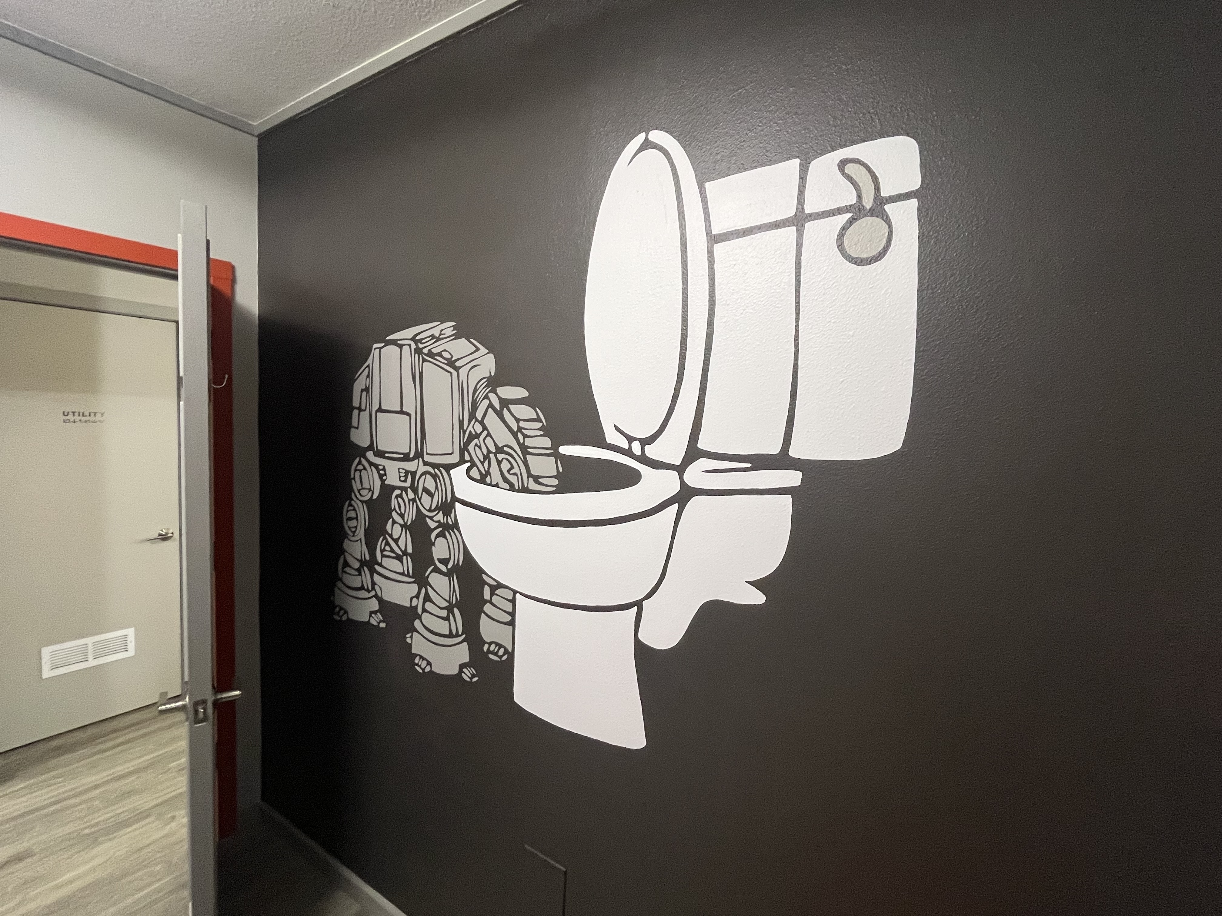 A wall mural of an AT-AT from Star Wars drinking out of the toilet like a dog.
