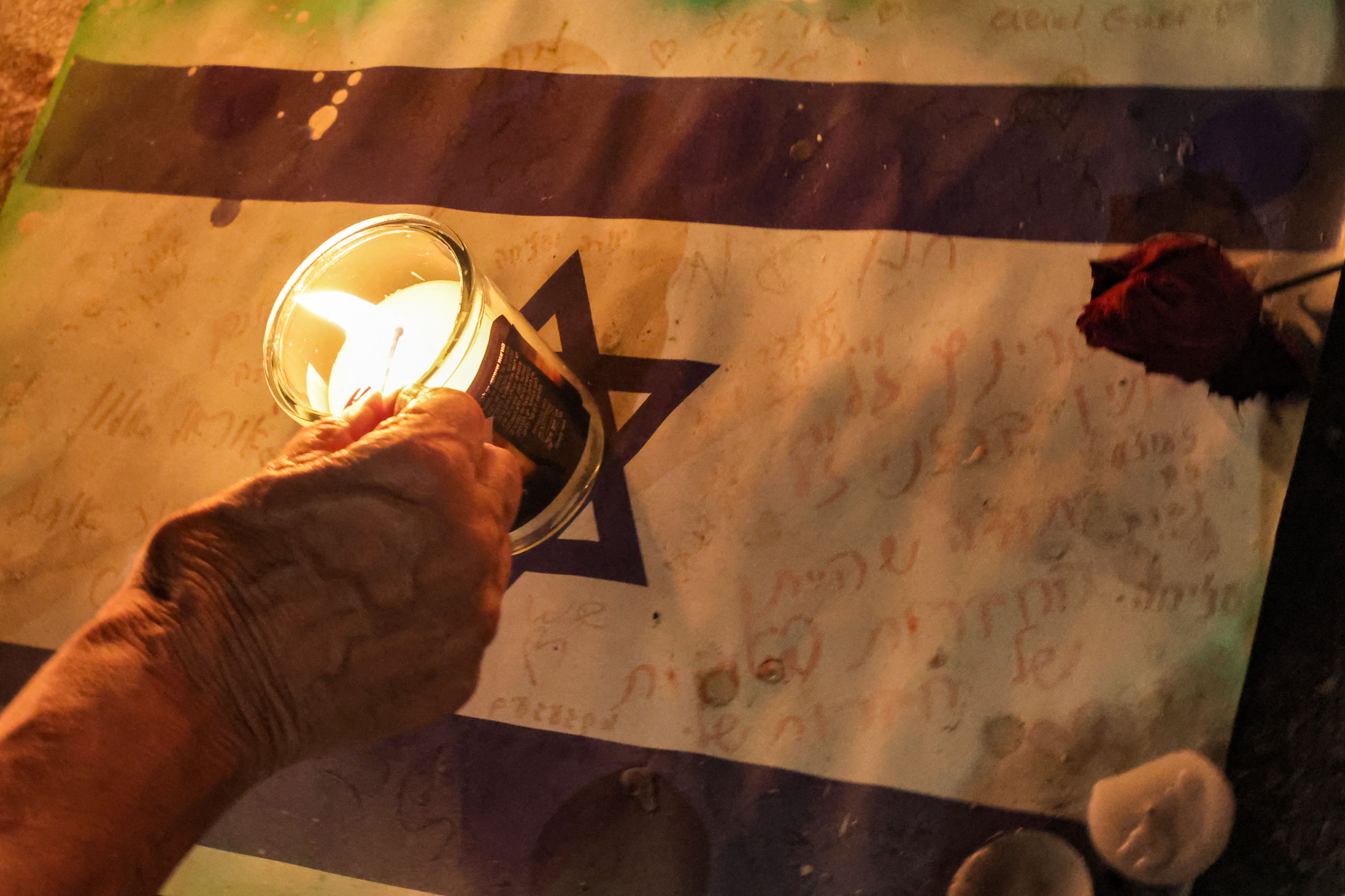 A woman lights a candle placed atop a sign showing an Israeli flag with hand-written notes on November 7, 2023, in Tel Aviv, Israel.