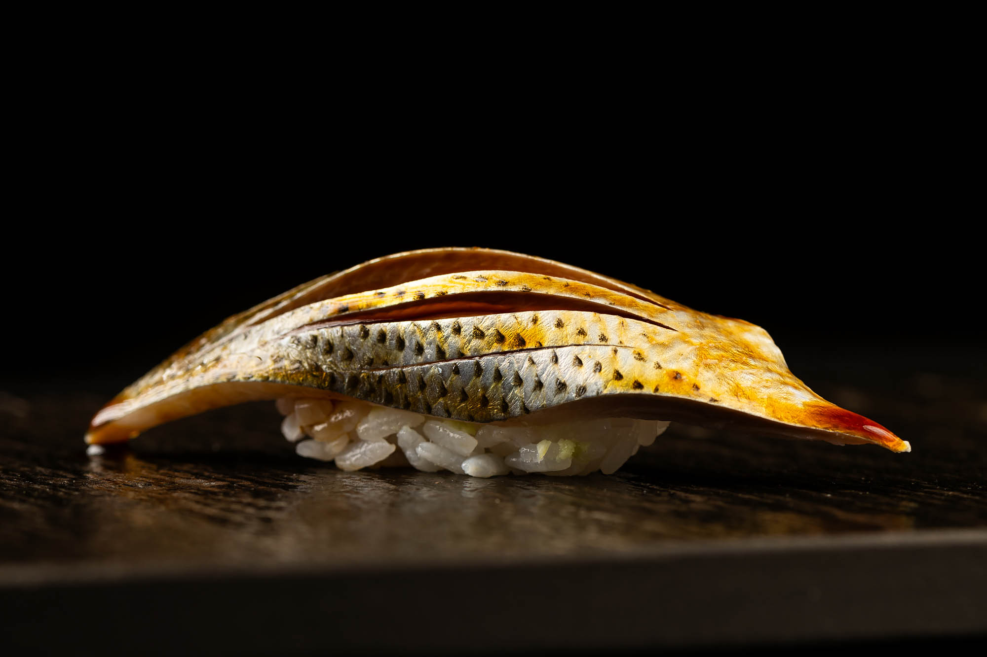 A piece of soy-sauce covered shad with slices inset over sushi rice.