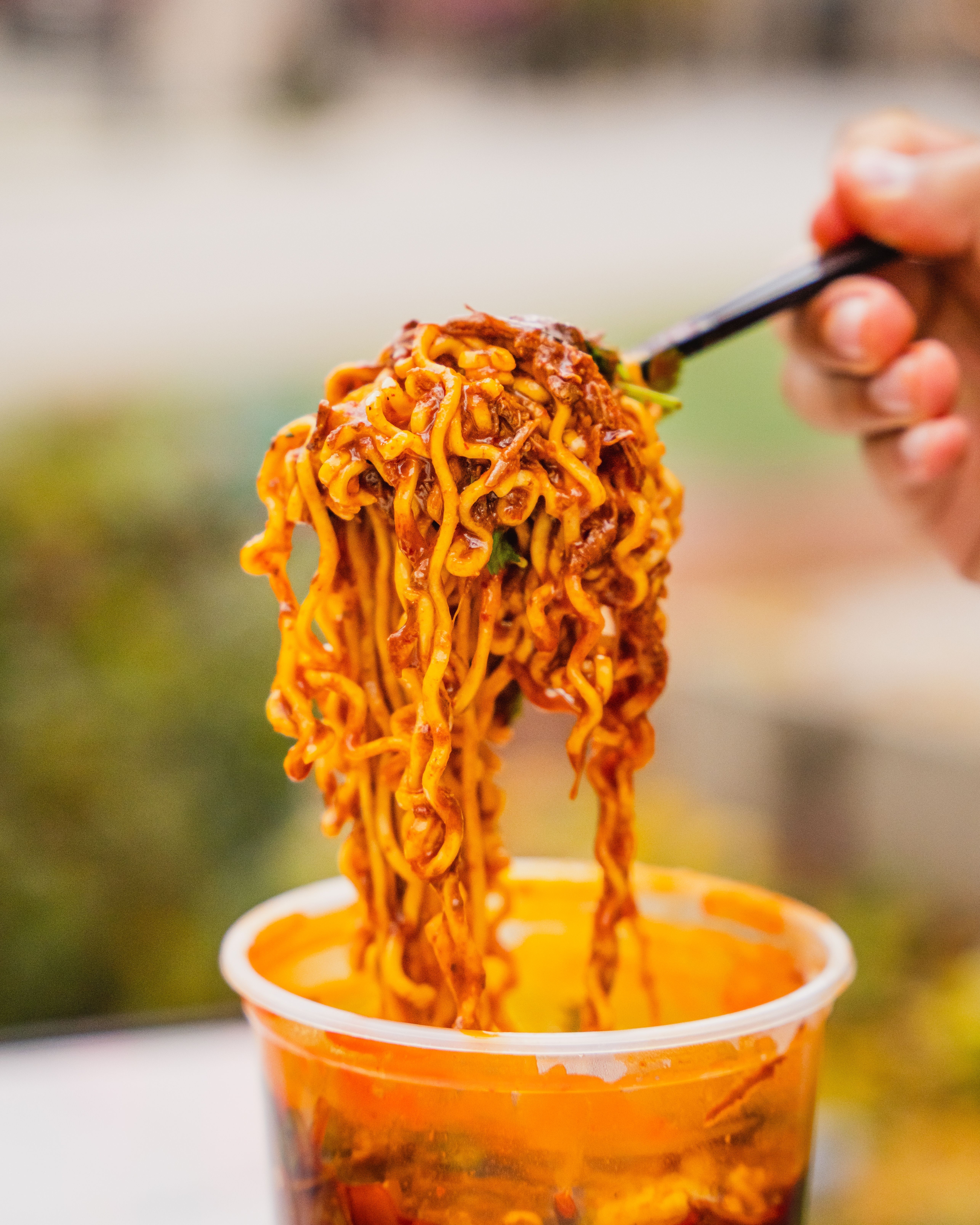 A forkful of red birria ramen being lifted out of a plastic quart container. 