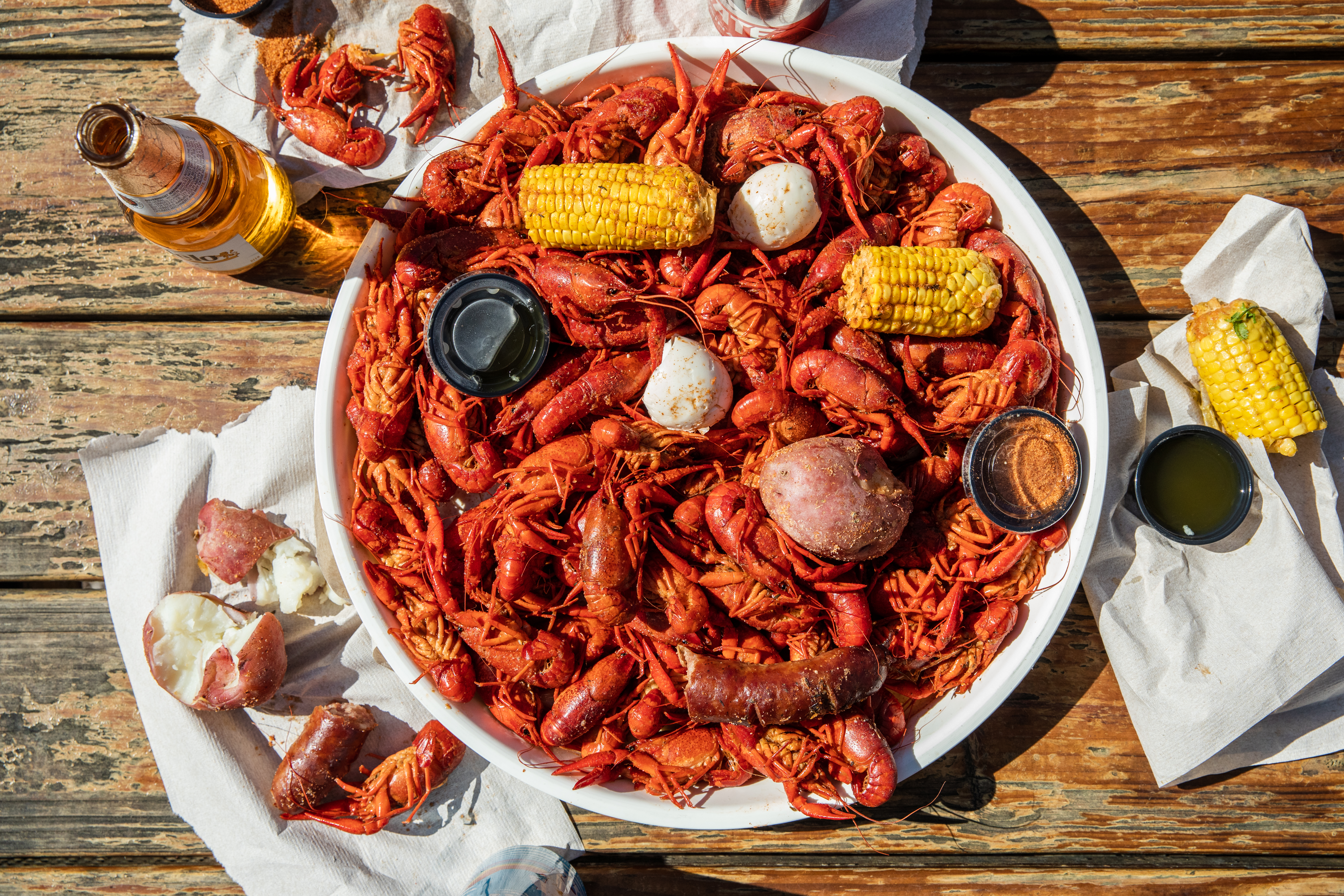 A metal tray of crawfish, with potatoes, hard-boiled eggs, corn on the cob, and bottles of beer.