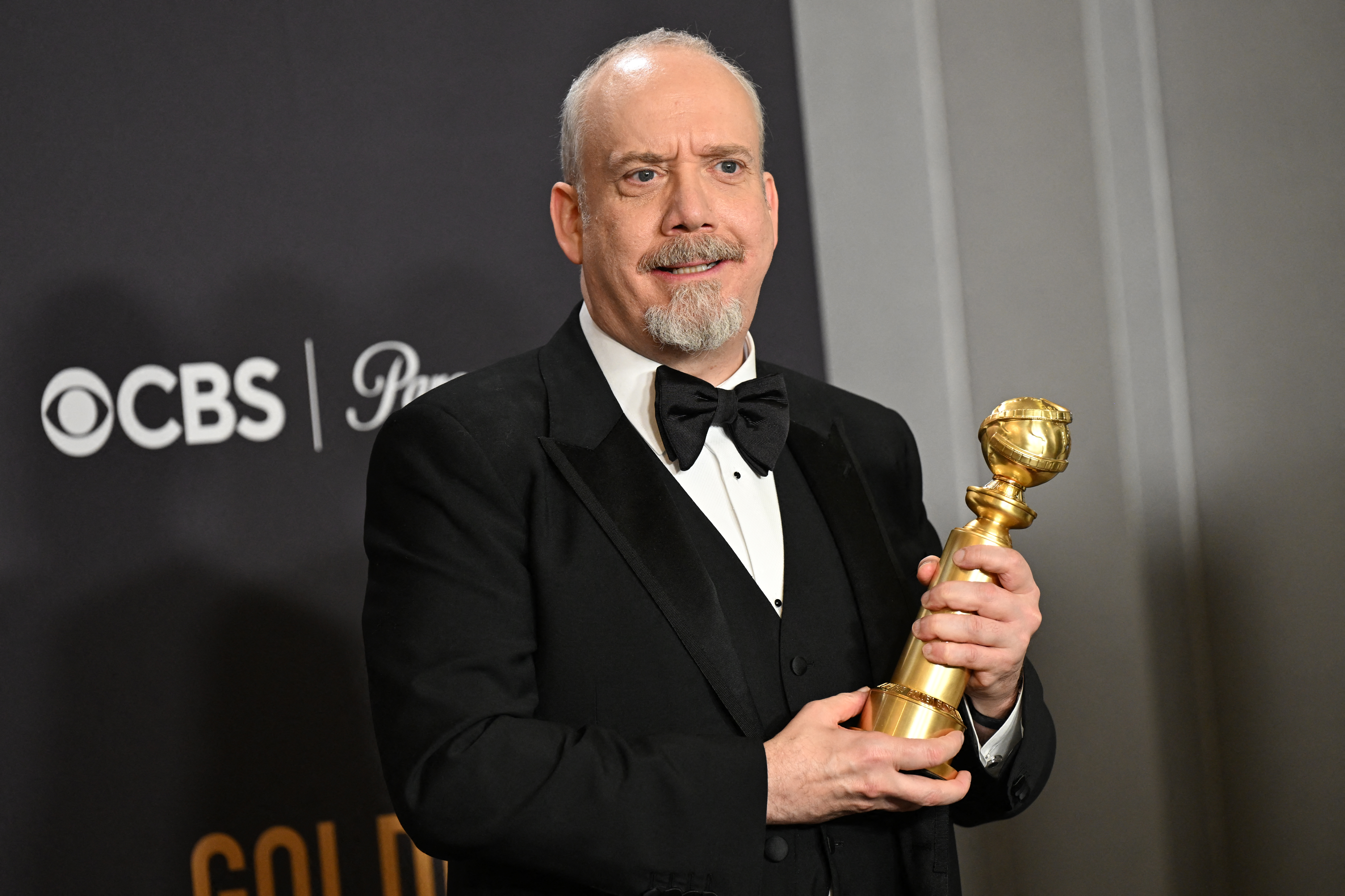 A male actor wearing a tuxedo poses with a Golden Globe award.