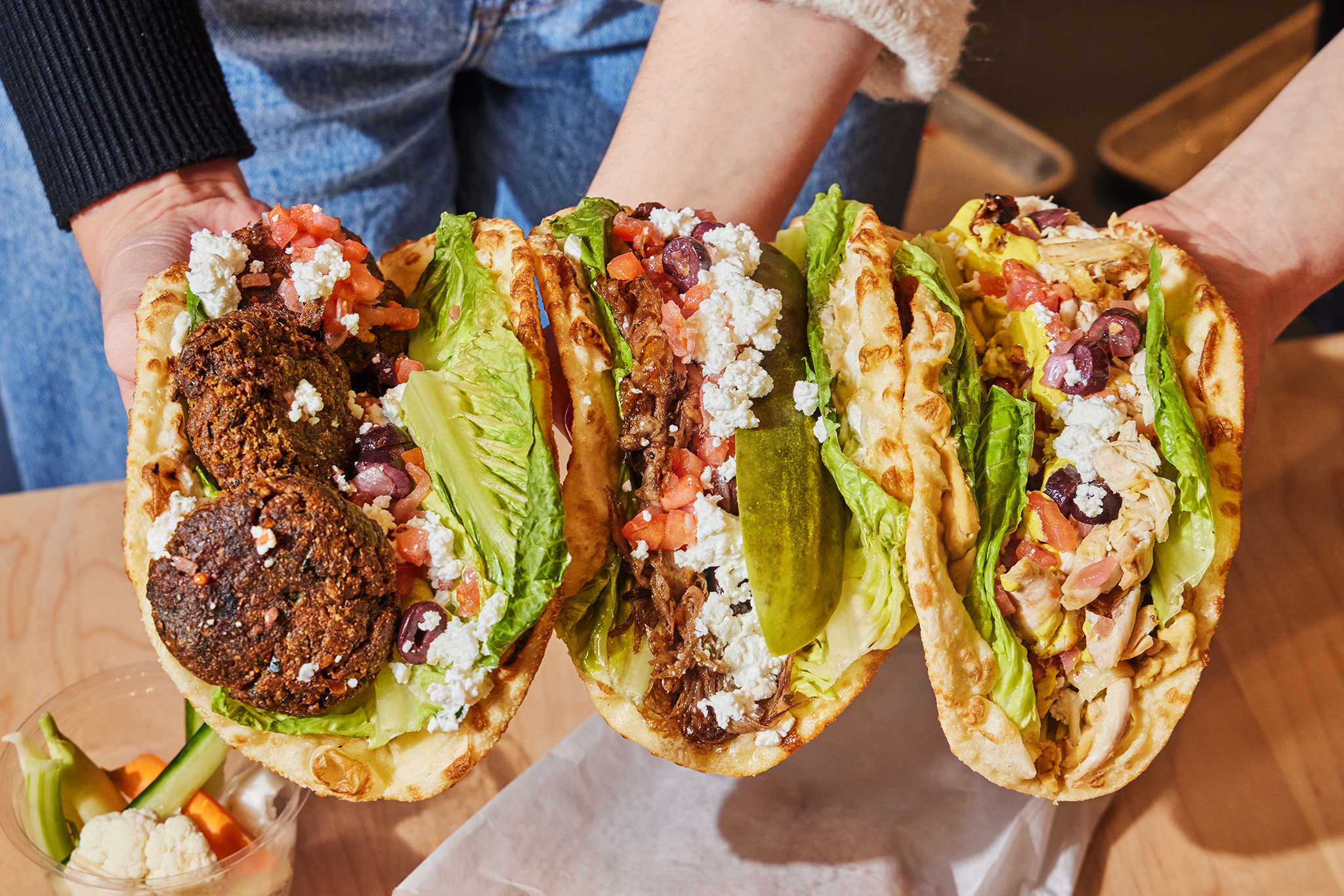 Three pita sandwiches held up and faced to the camera to reveal fillings including falafel, cheese, and lettuces.