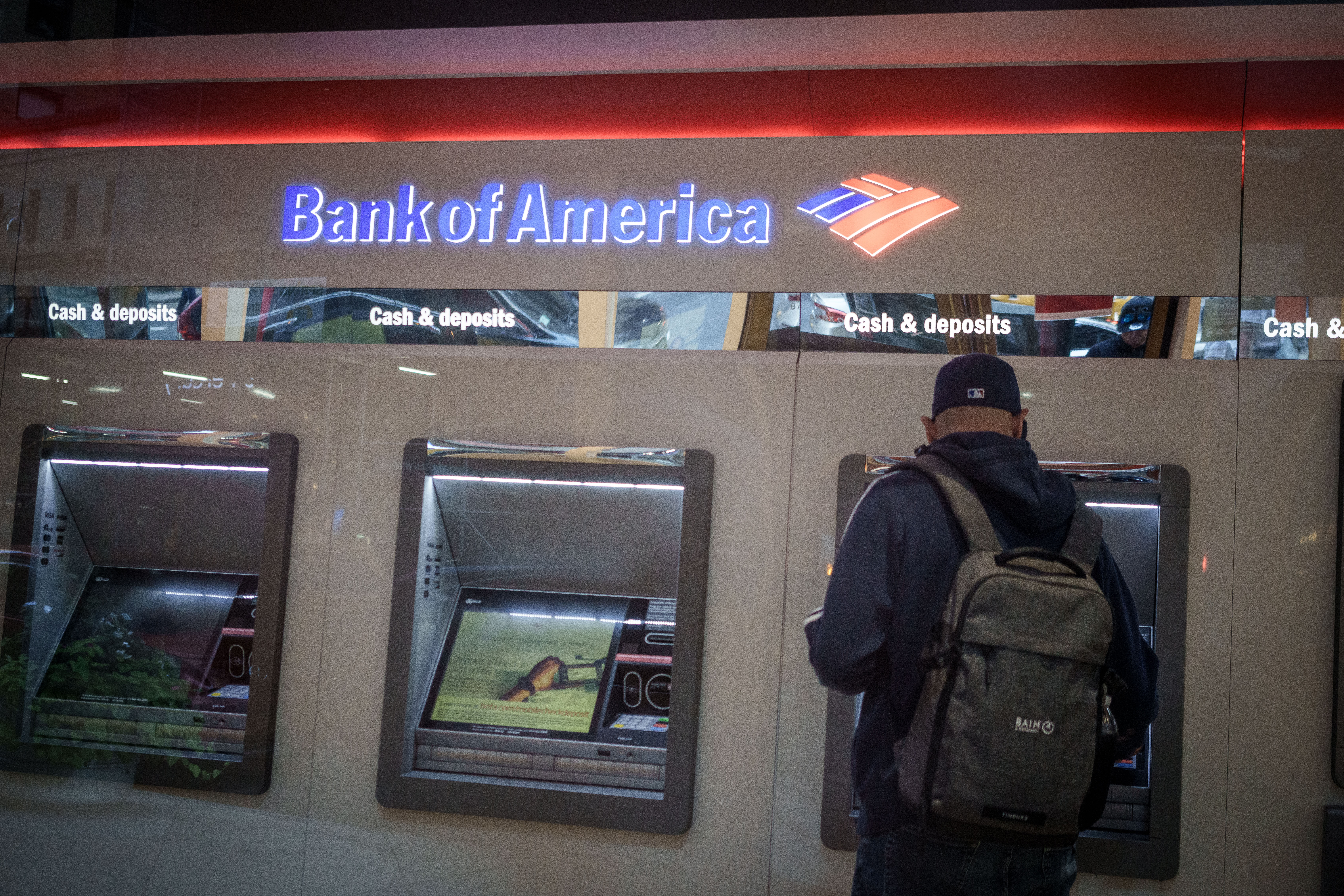 A person carrying a backpack stands at a Bank of America ATM.