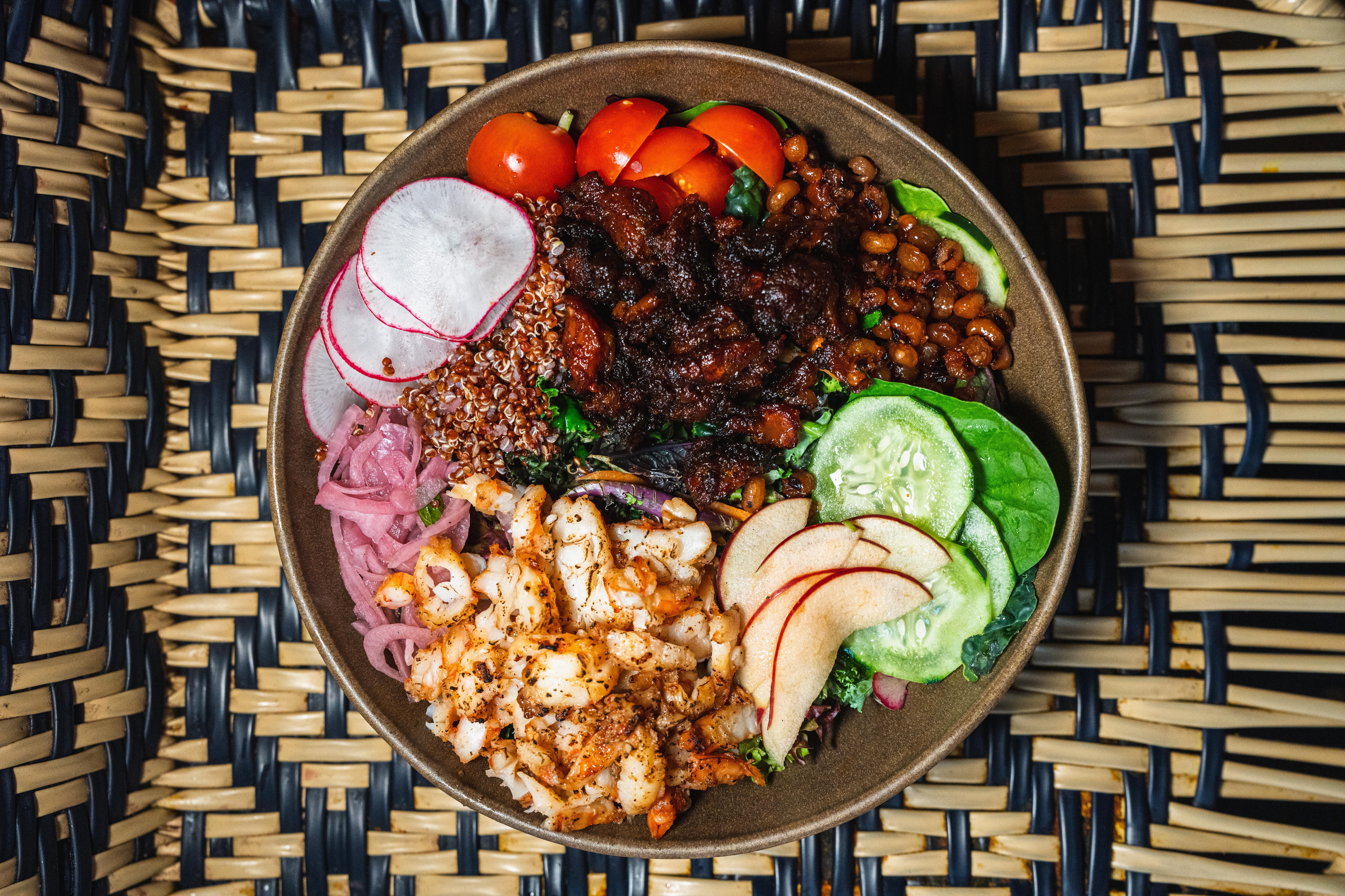 A bowl of chicken, pickled onions, tomatoes, lettuce, tomato, apples, radish, vegetables, and quinoa from ChopnBlok.