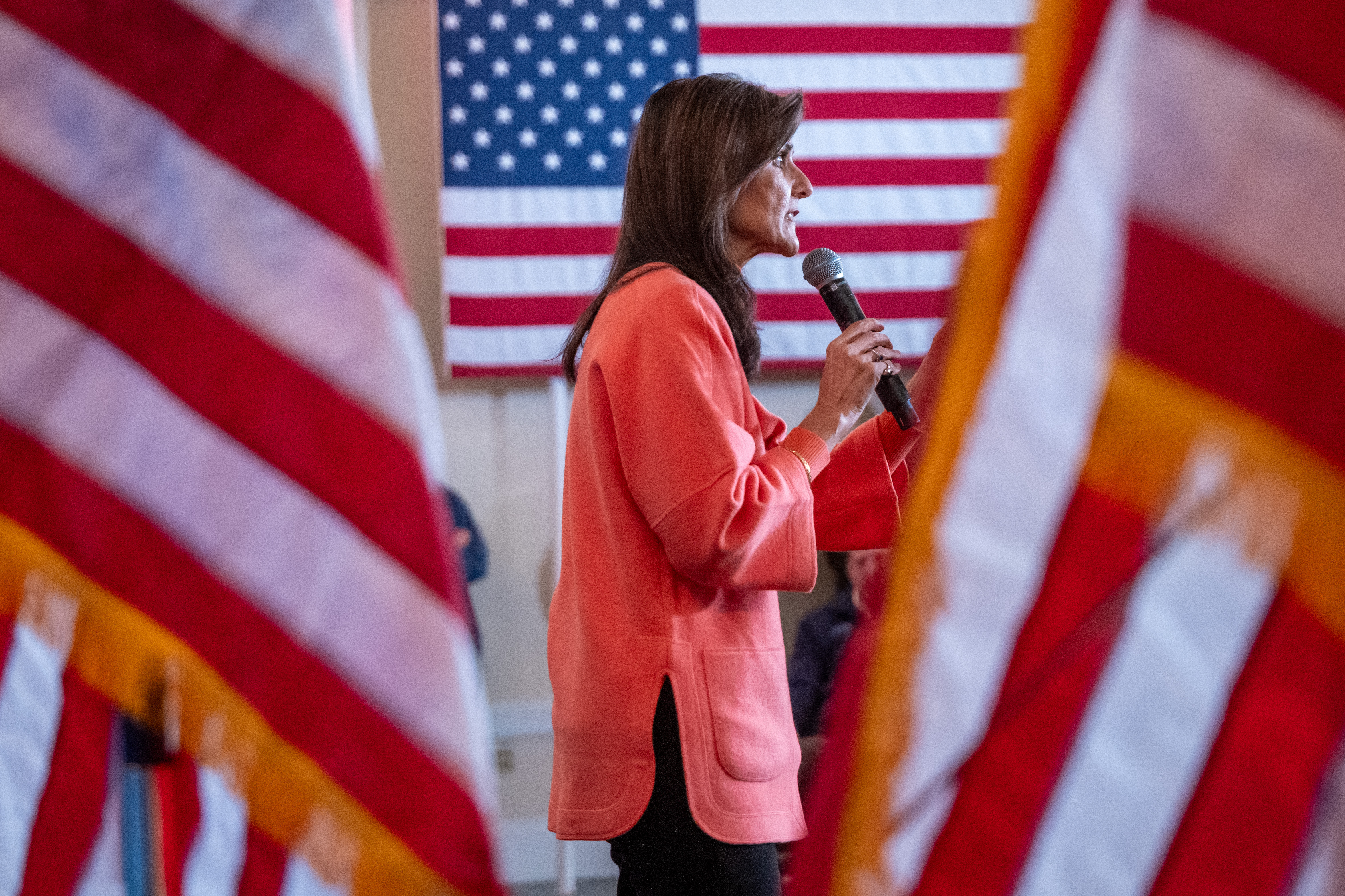 Nikki Haley speaking into a microphone and surrounded by American flags at a campaign stop in New Hampshire.