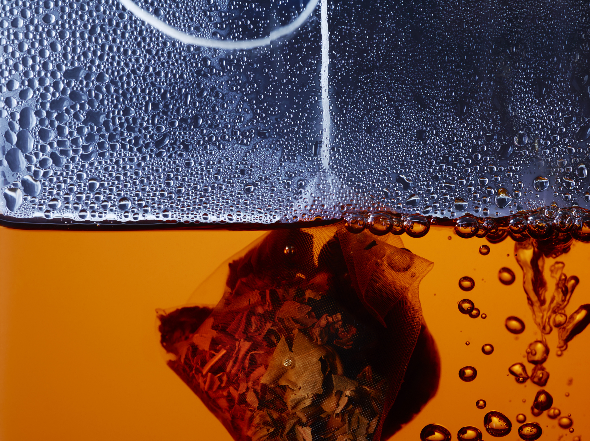 A close-up shot of a tea bag steeping in a transparent mug, with condensation forming on the cup’s side.