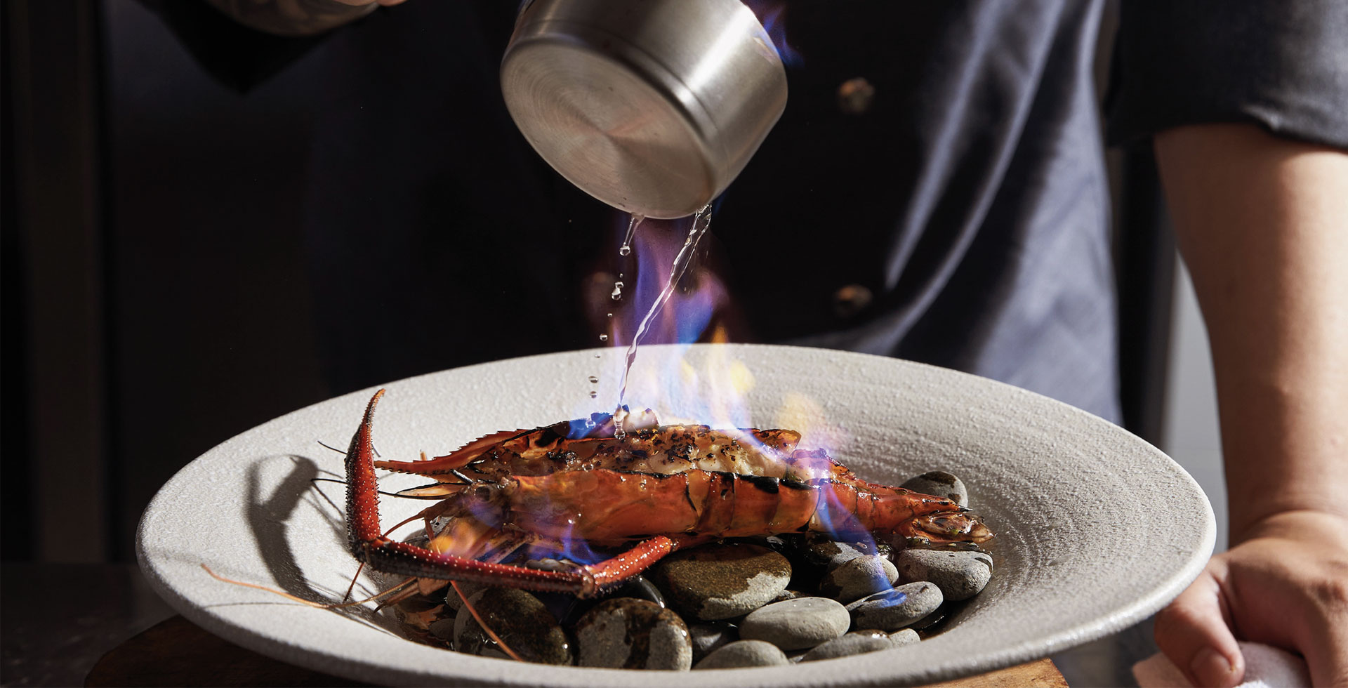 A lobster in a shallow plate being doused in fire.