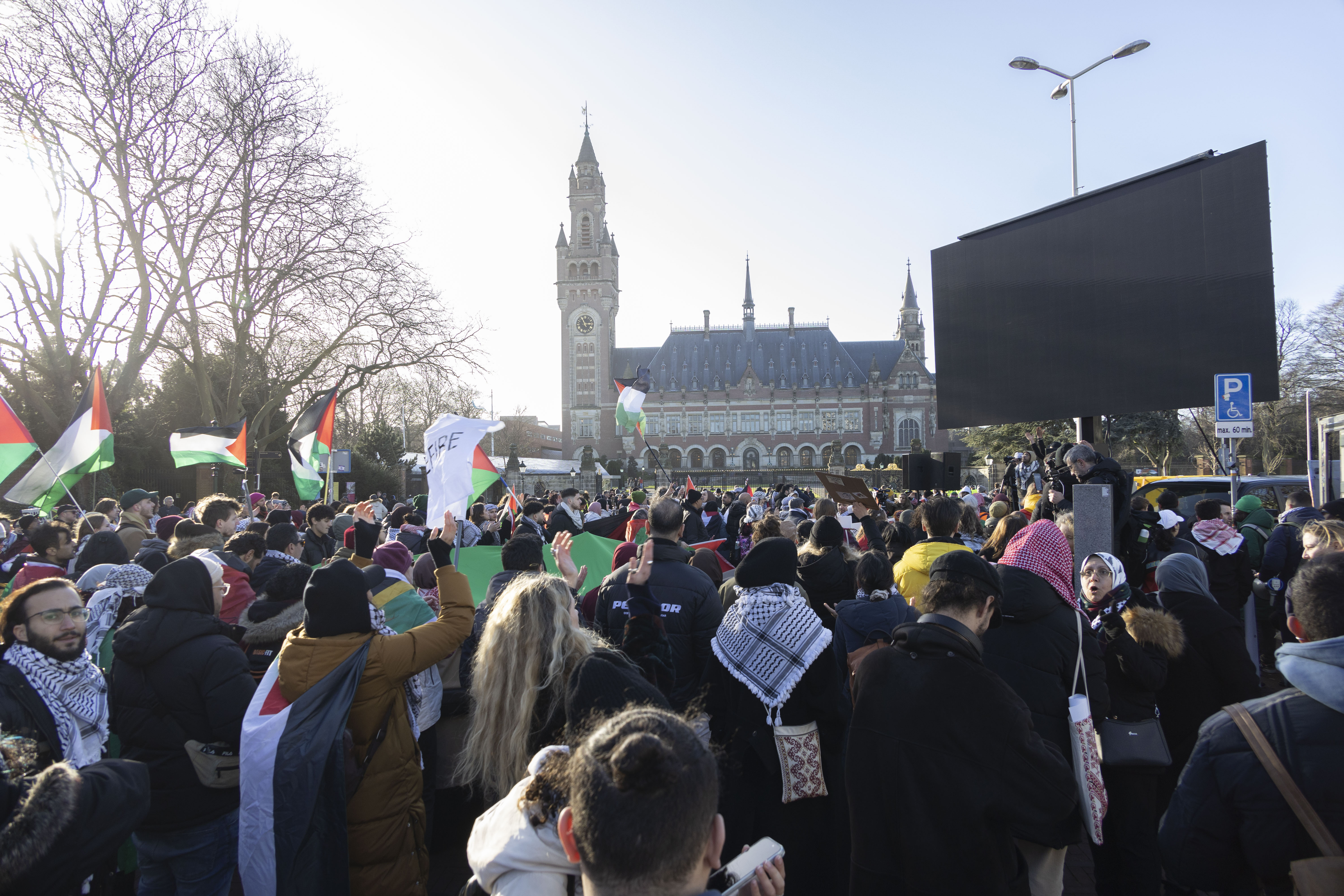 People, holding Palestinian flags, gather outside the International Court of Justice.