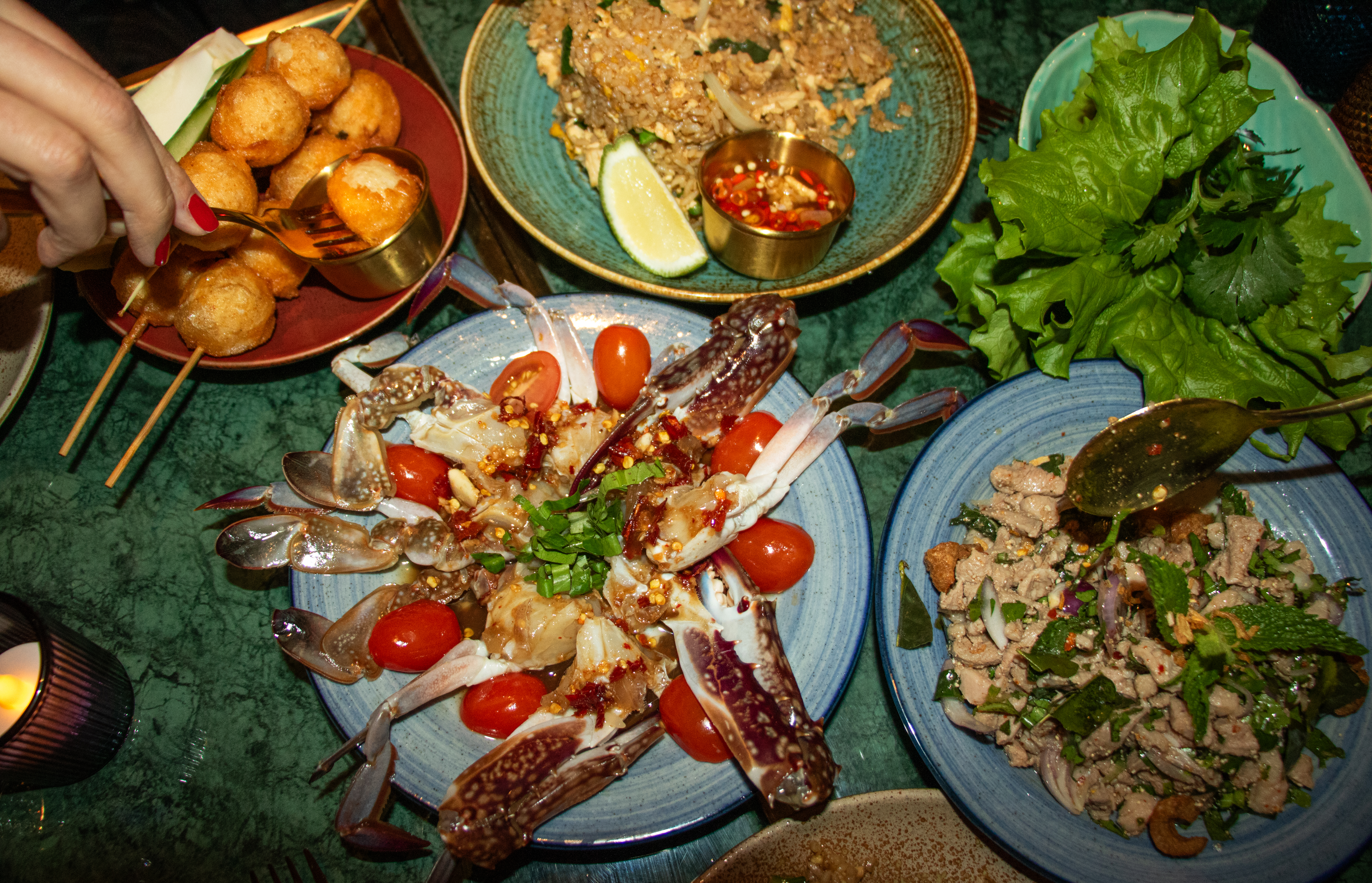 An overhead photograph of a crowded table with raw fermented crab, fried meatballs, and duck salad.