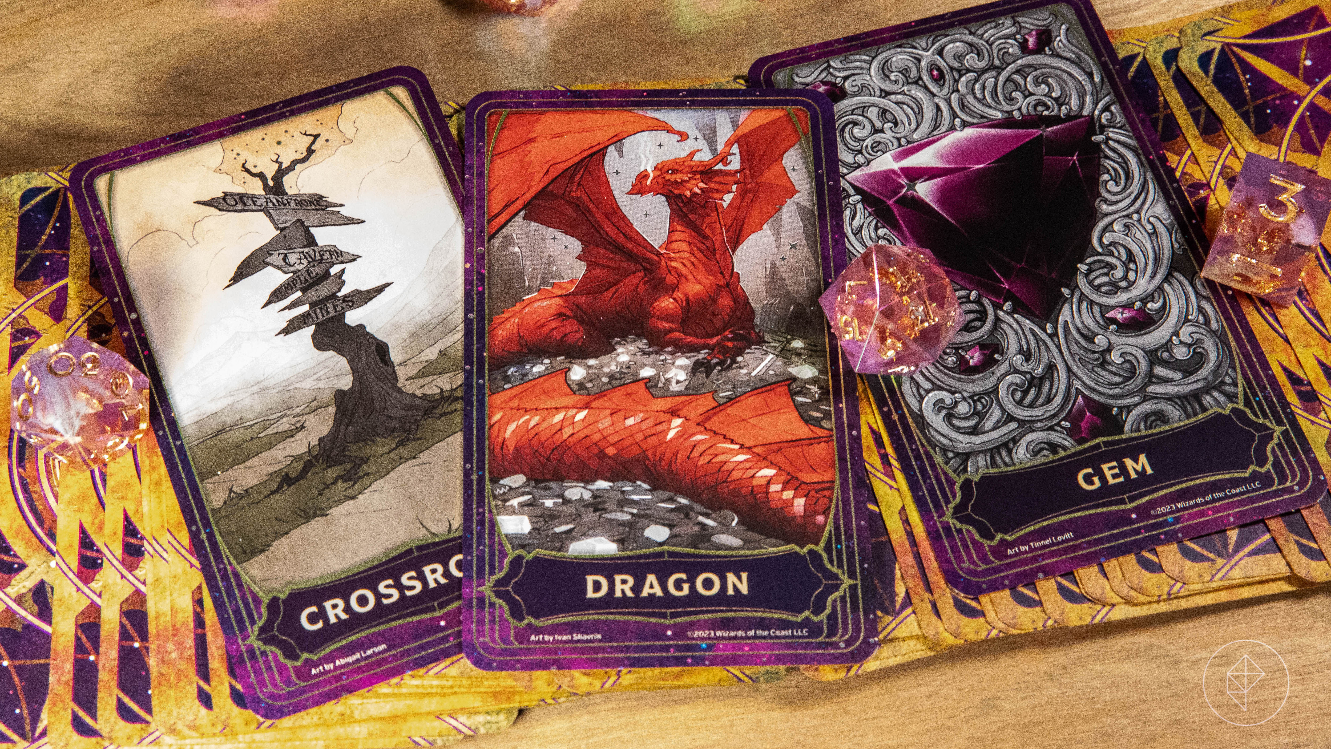 Three face-up cards, including crossroads, dragon, and gem, sit atop a deck of cards that are face down, with pink dice on top of them.