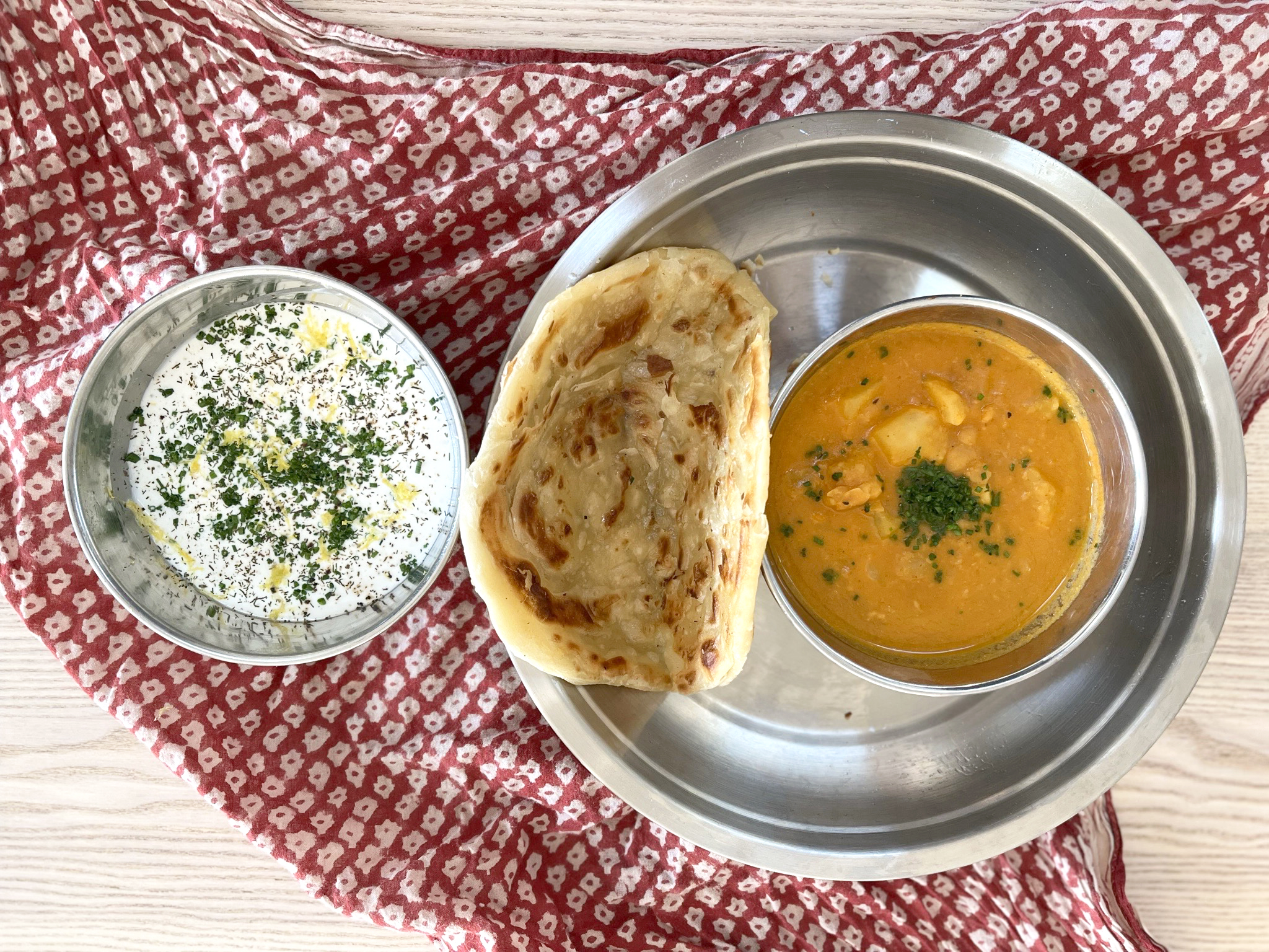 A tin bowl of a flatbread with another bowl of orange sauce next to a bowl of white sauce with green herbs.