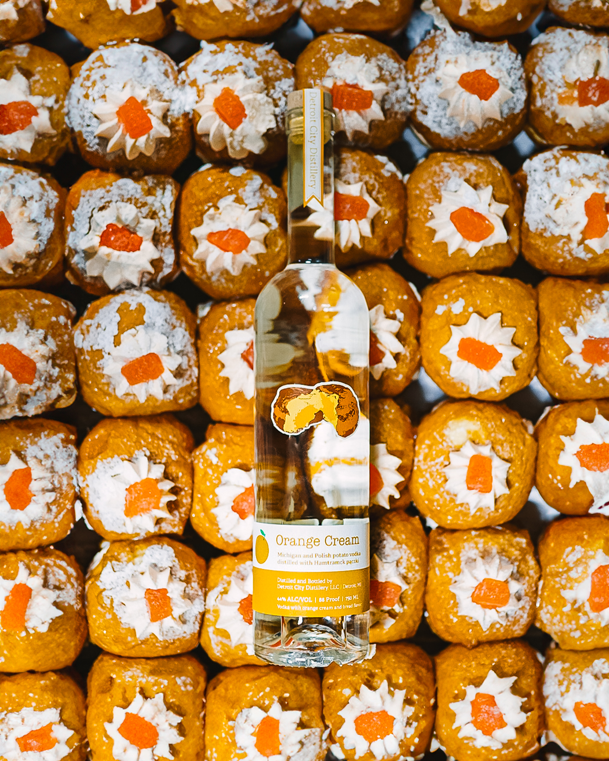 Orange cream paczki with jelly and creaming popping out of the top and a clear bottle of vodka with orange and white labels.