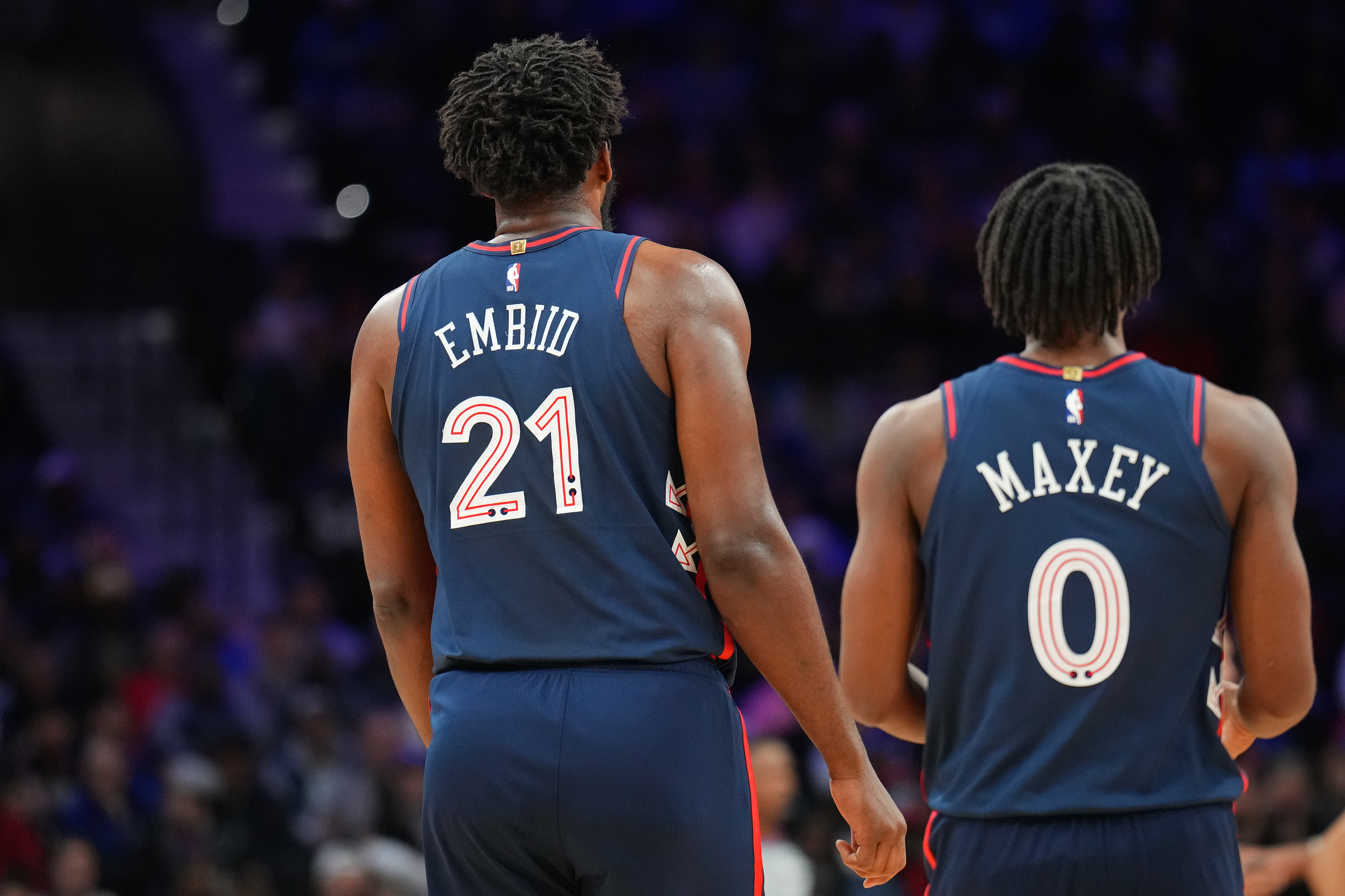 View from behind of Joel Embiid standing next to Tyrese Maxey. 