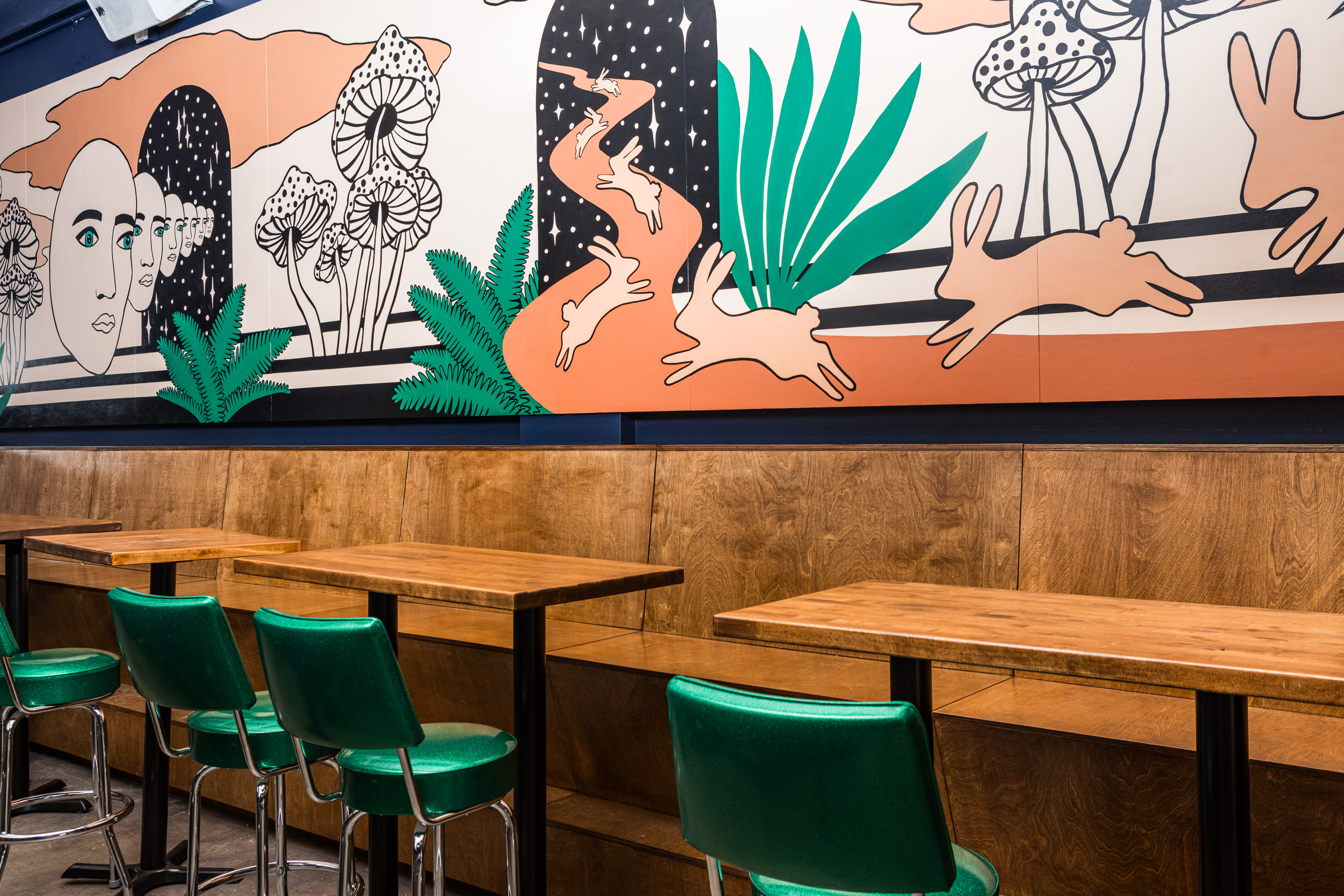 The interior of a bar with an art deco–style mural that shows rabbits running through a dessert among other things.