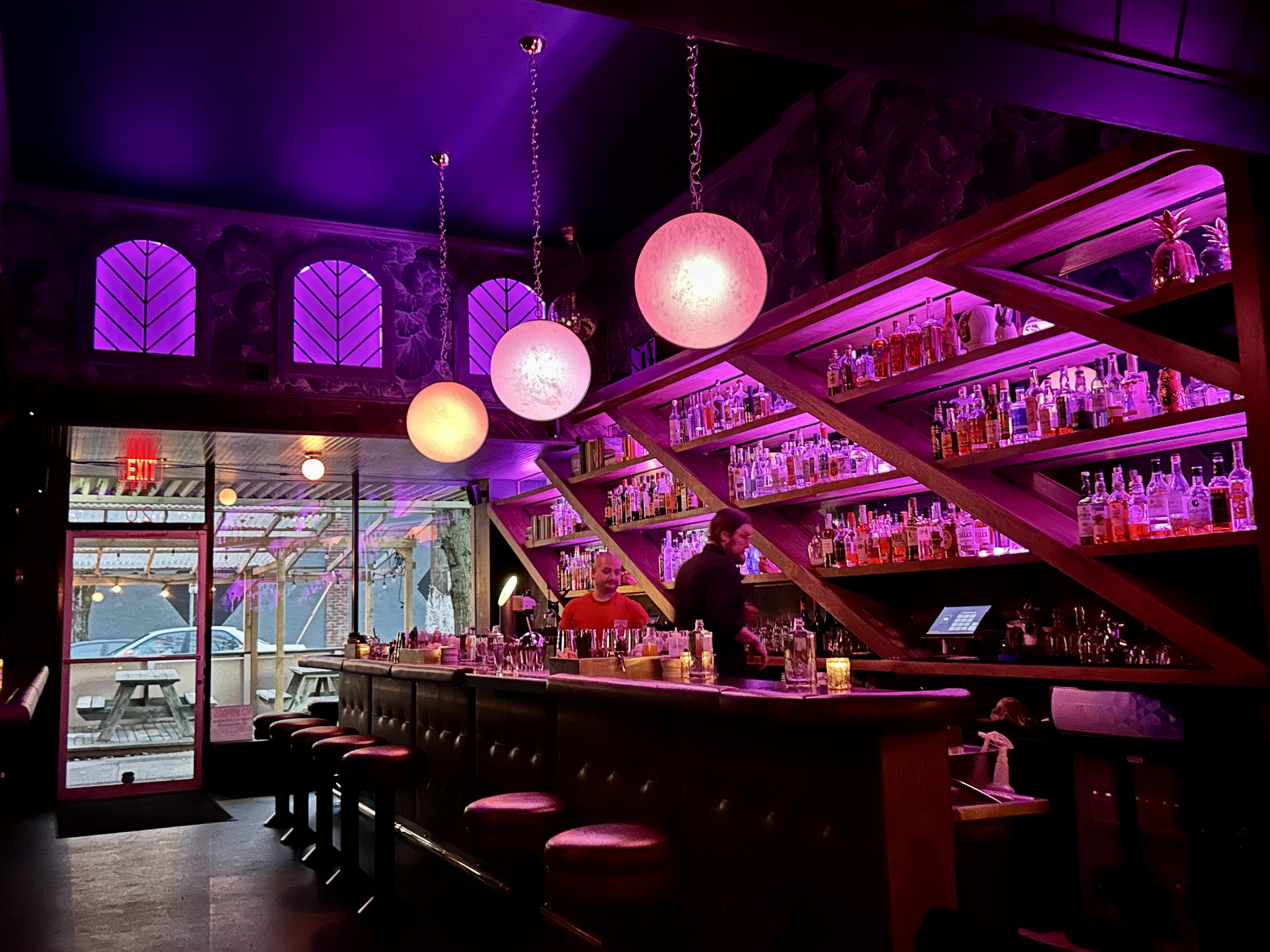 The interior of a bar with pink and purple lighting.