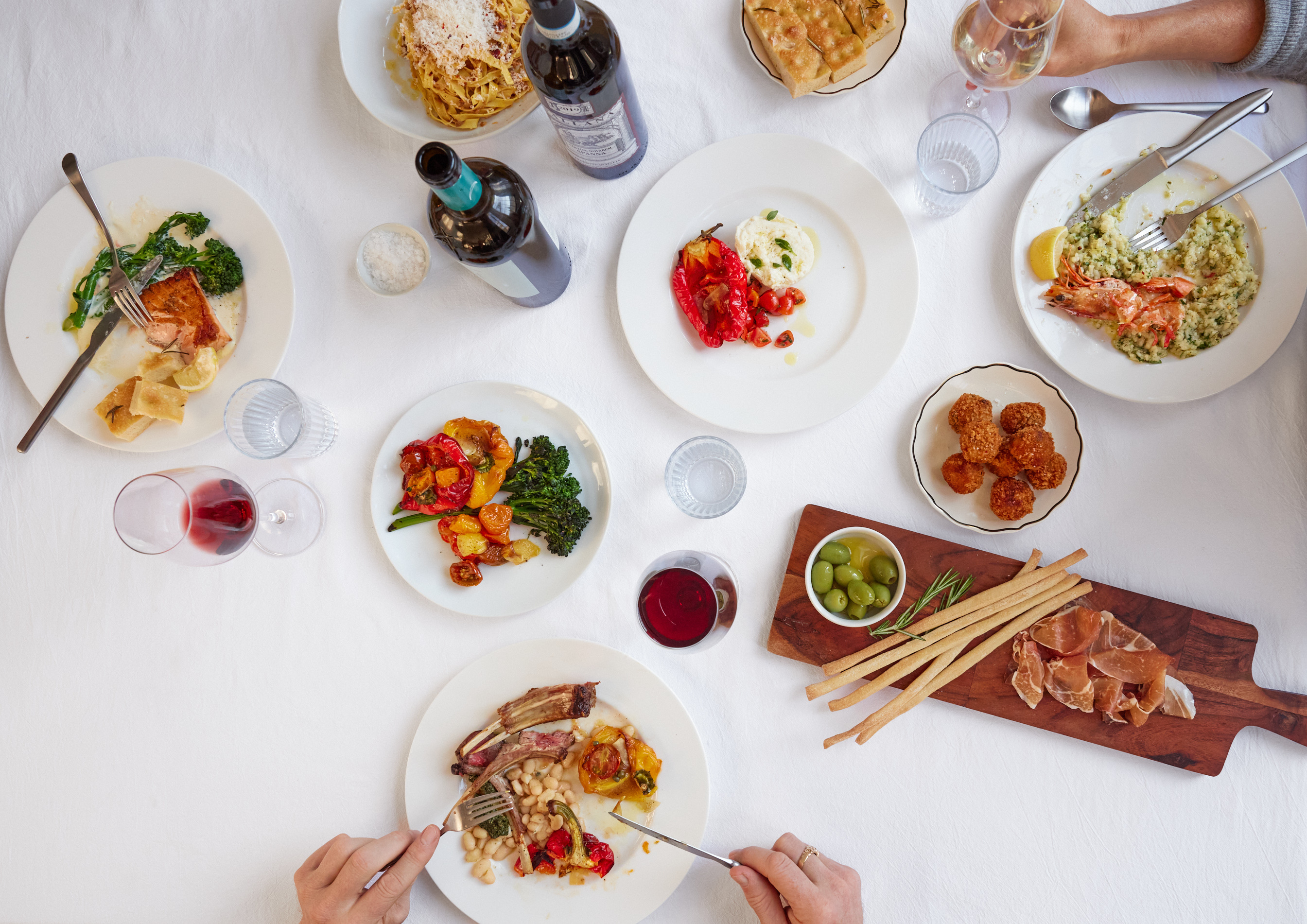 An aerial view of assorted Italian dishes on white plates on a white background. 