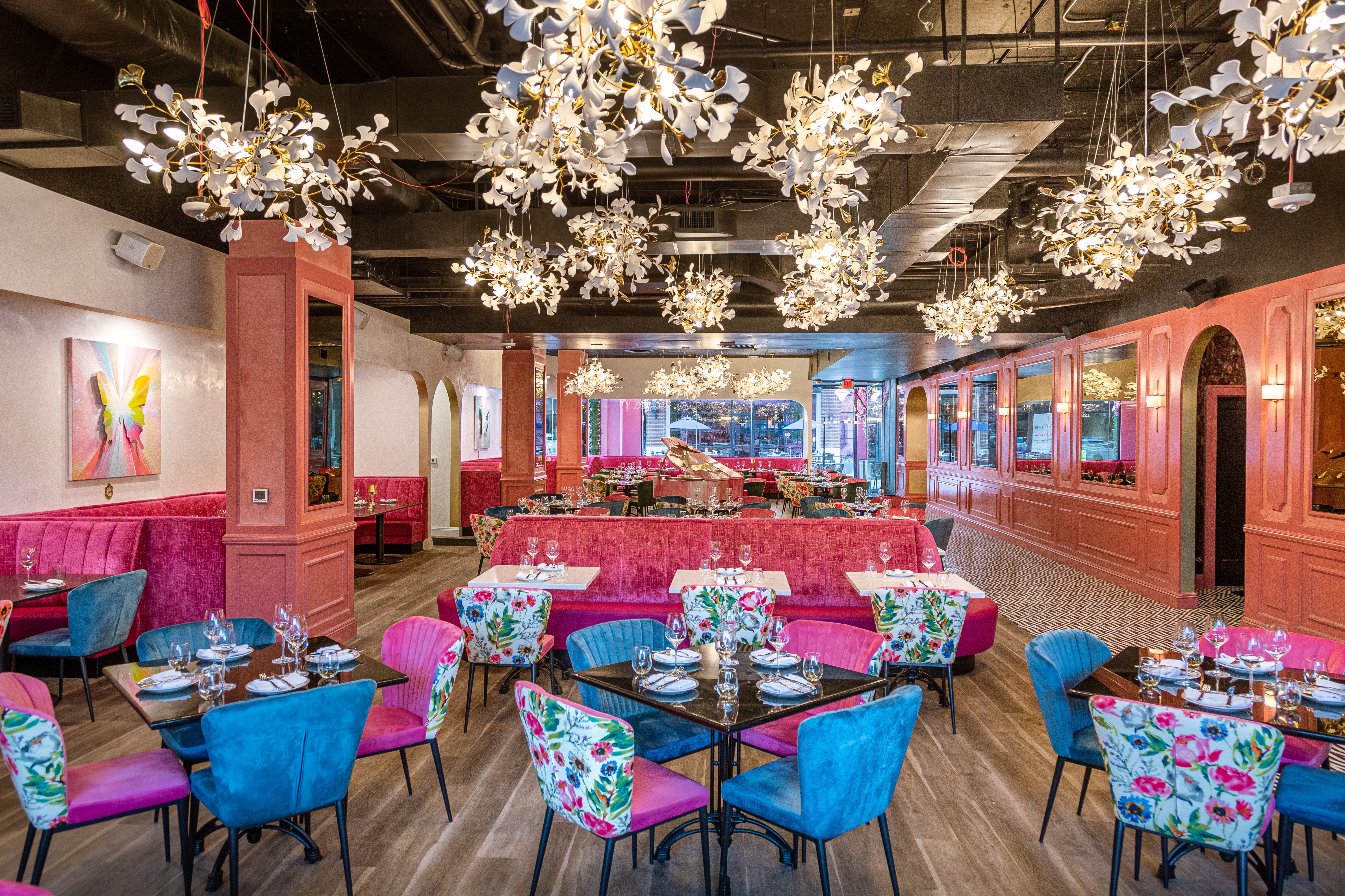 A dining room with pink and blue chairs, neon pink booths, lighter pink walls, and several chandeliers. 