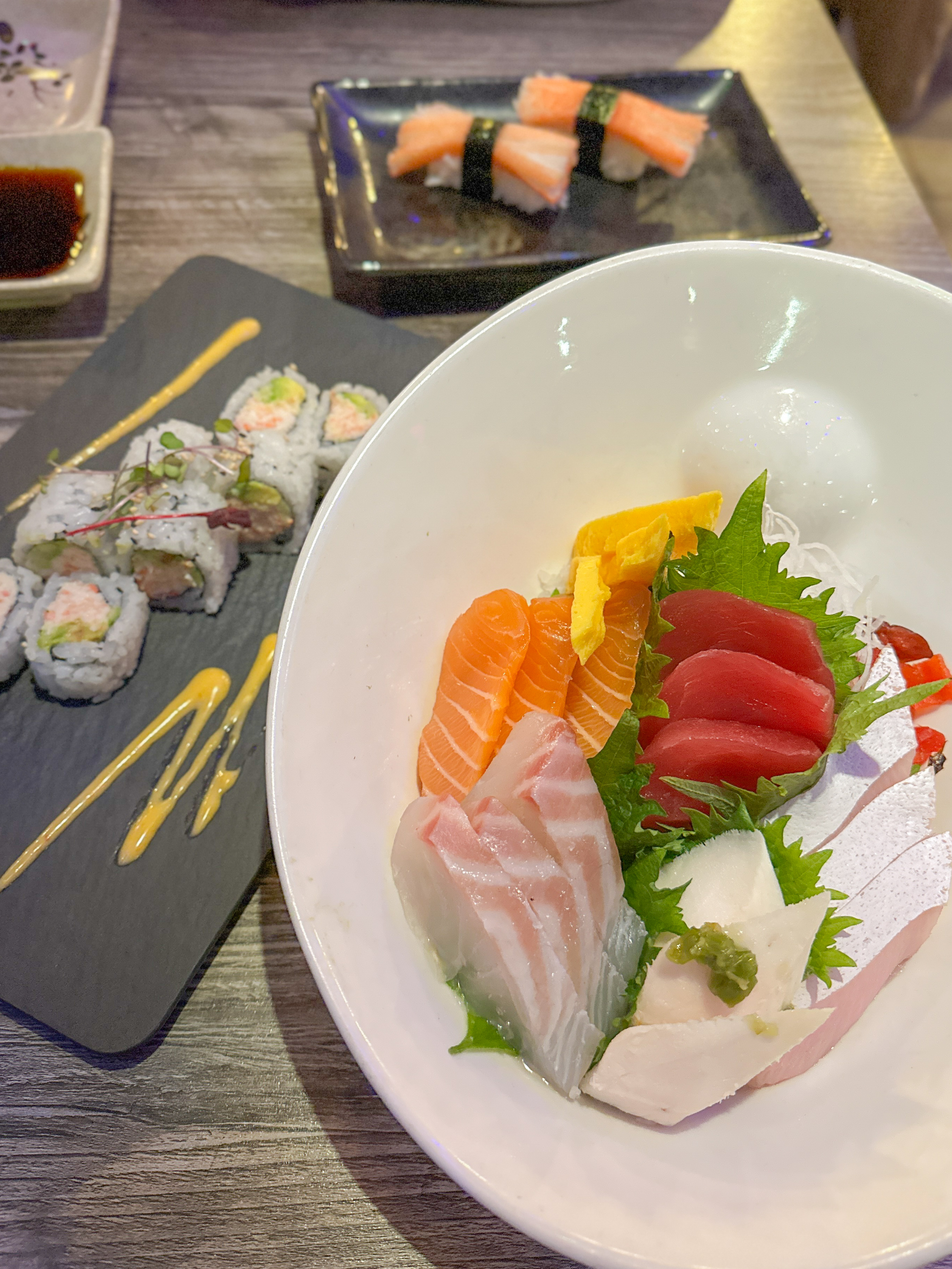 A plate of nigri sushi sits on a table, with a dish of sushi rolls next to it.