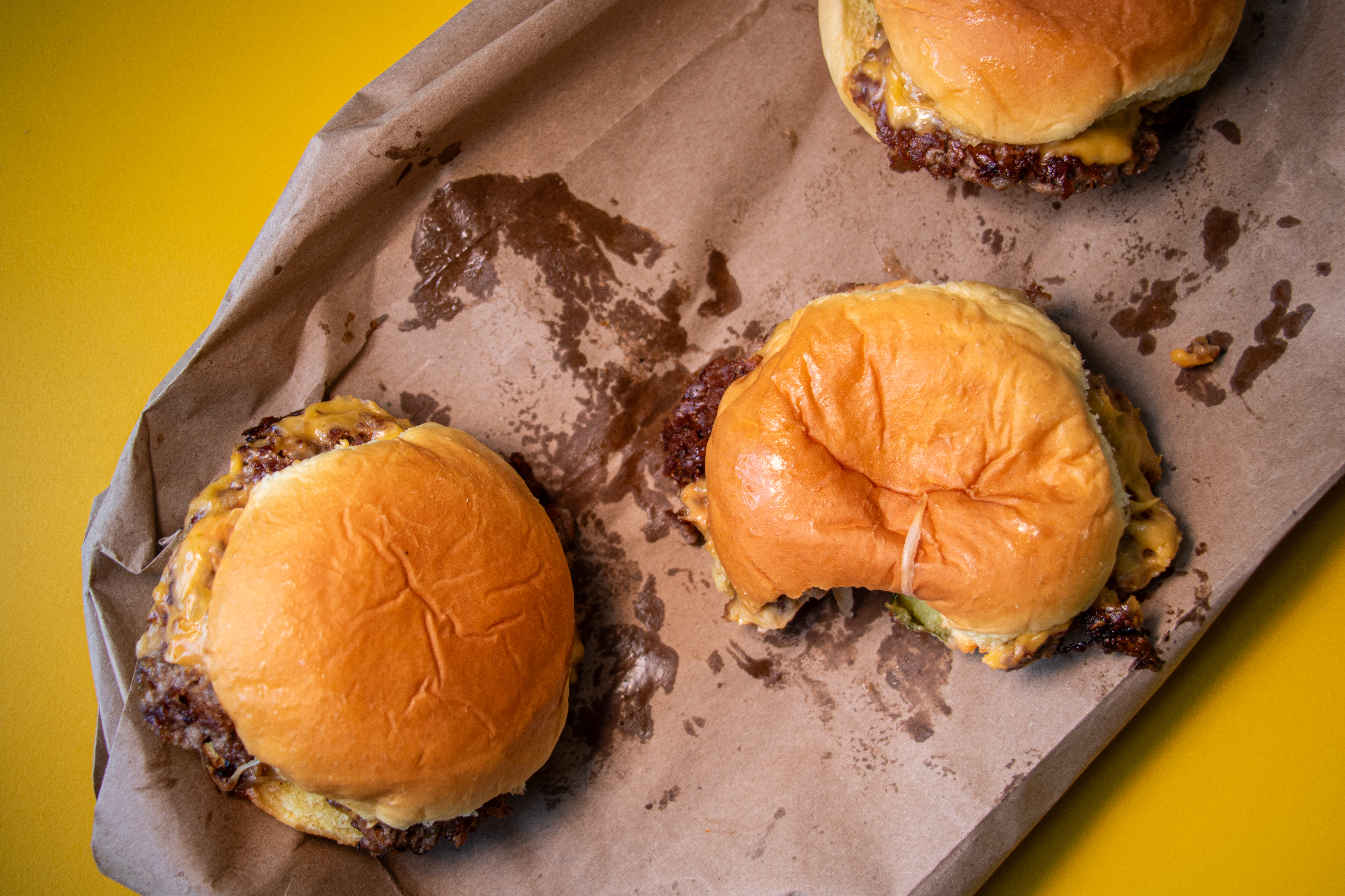 An overhead photograph of three small burgers on a greasy paper bag.